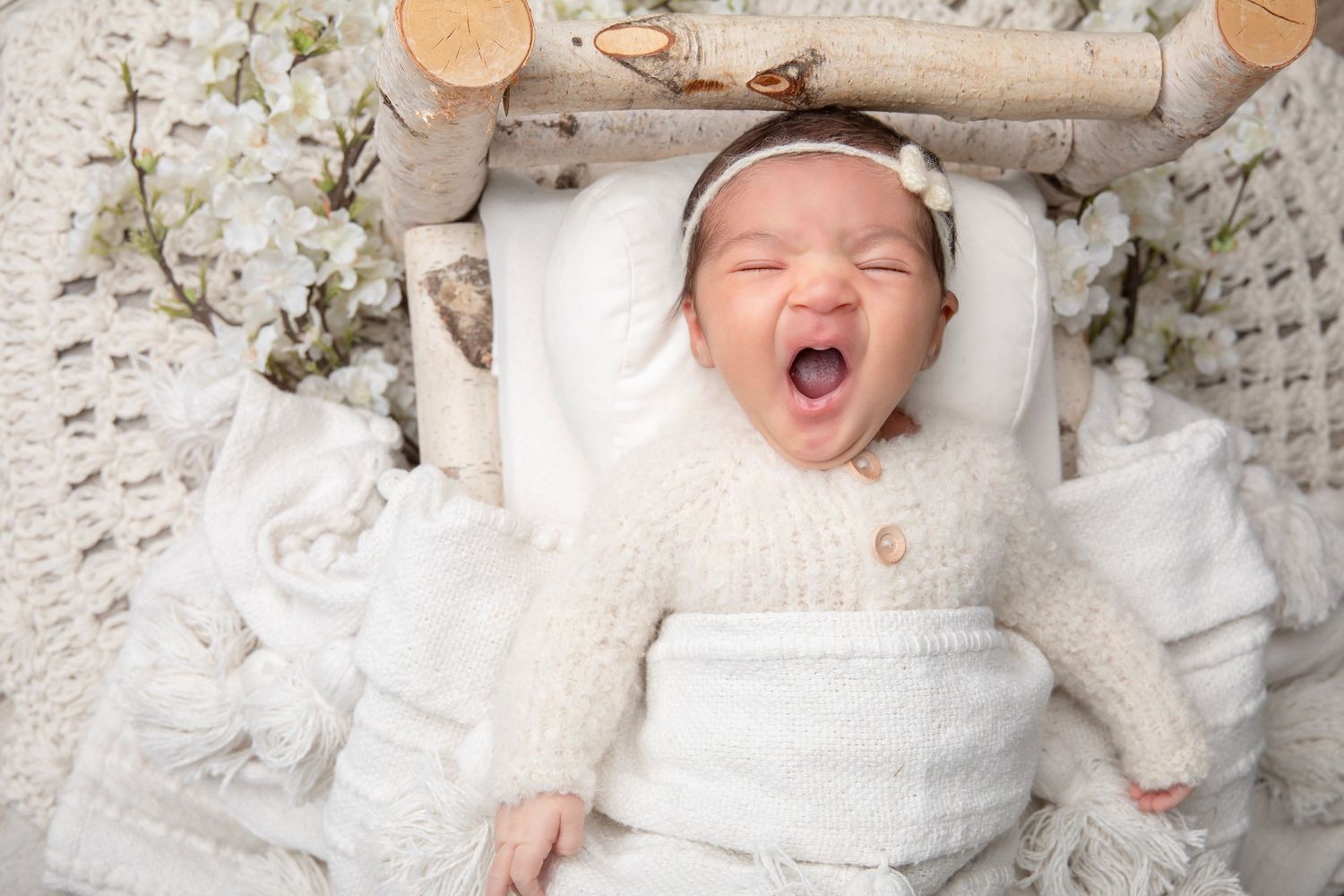 Sweet newborn photography set against floral backdrop with soft white wrapping.