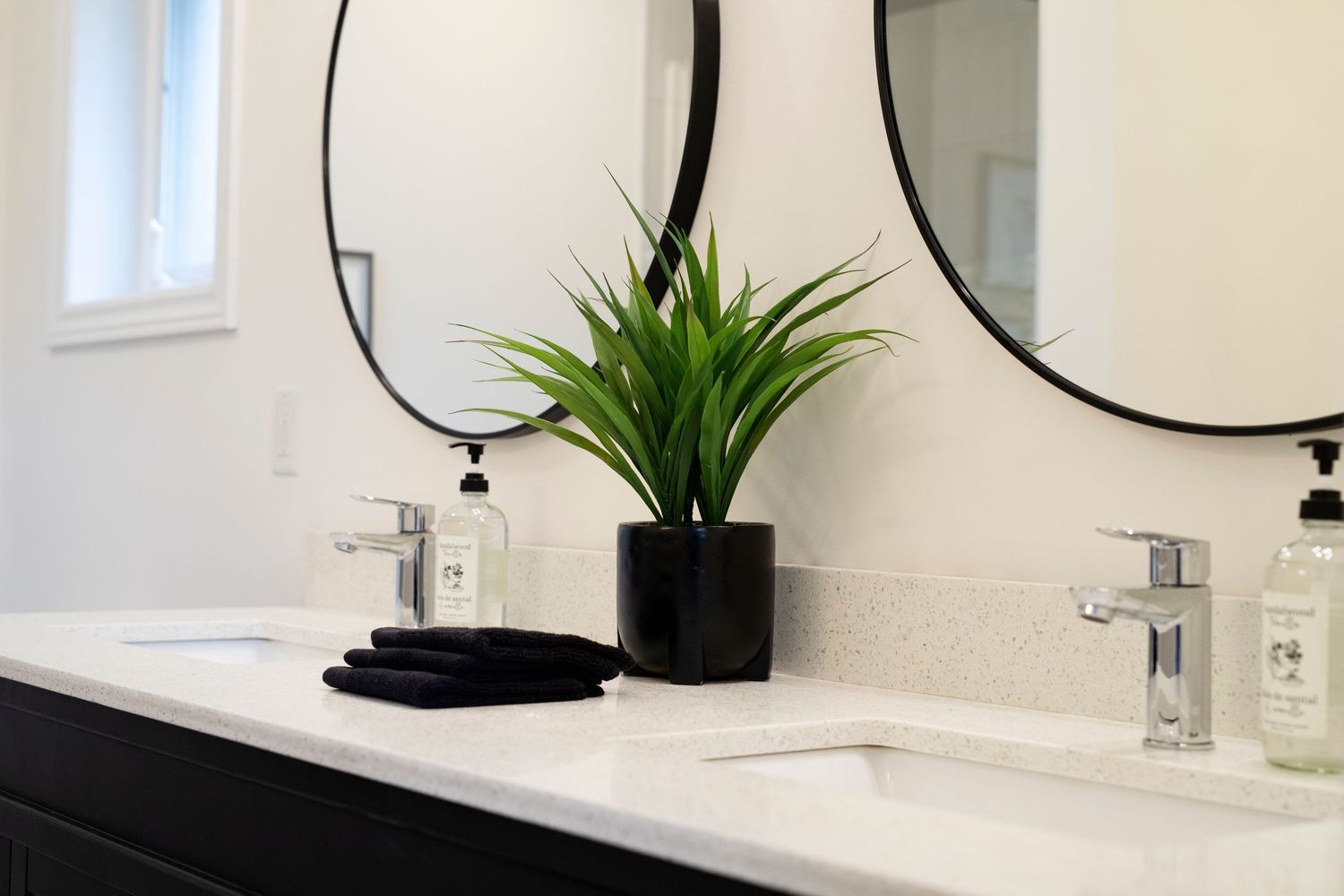 Modern bathroom vanity with dual oval mirrors, black cabinets, white countertops, and a decorative potted plant.