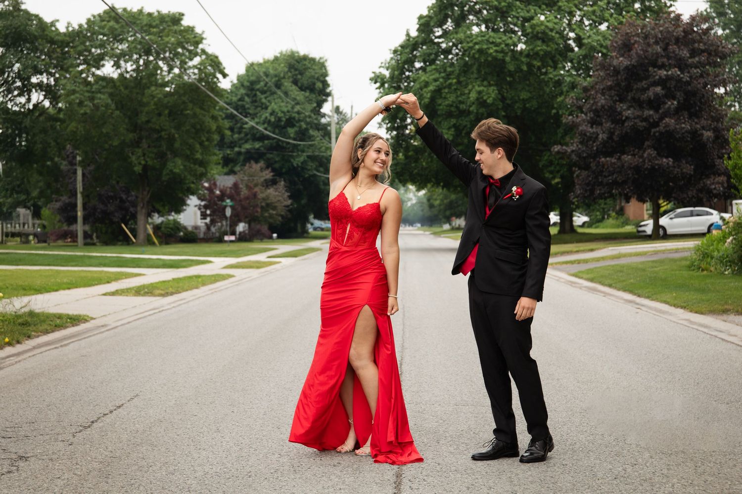 A graduating couple dancing on a residential street, with the woman in a flowing red gown.