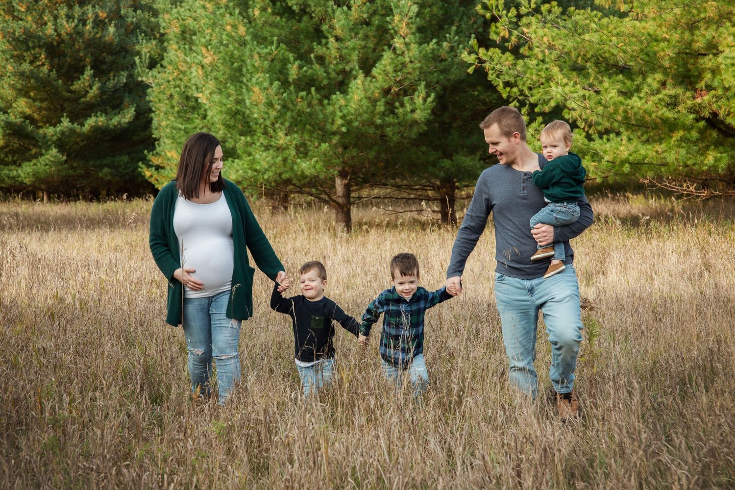 A family photo session in a rustic outdoor field with tall grass and trees in the background.