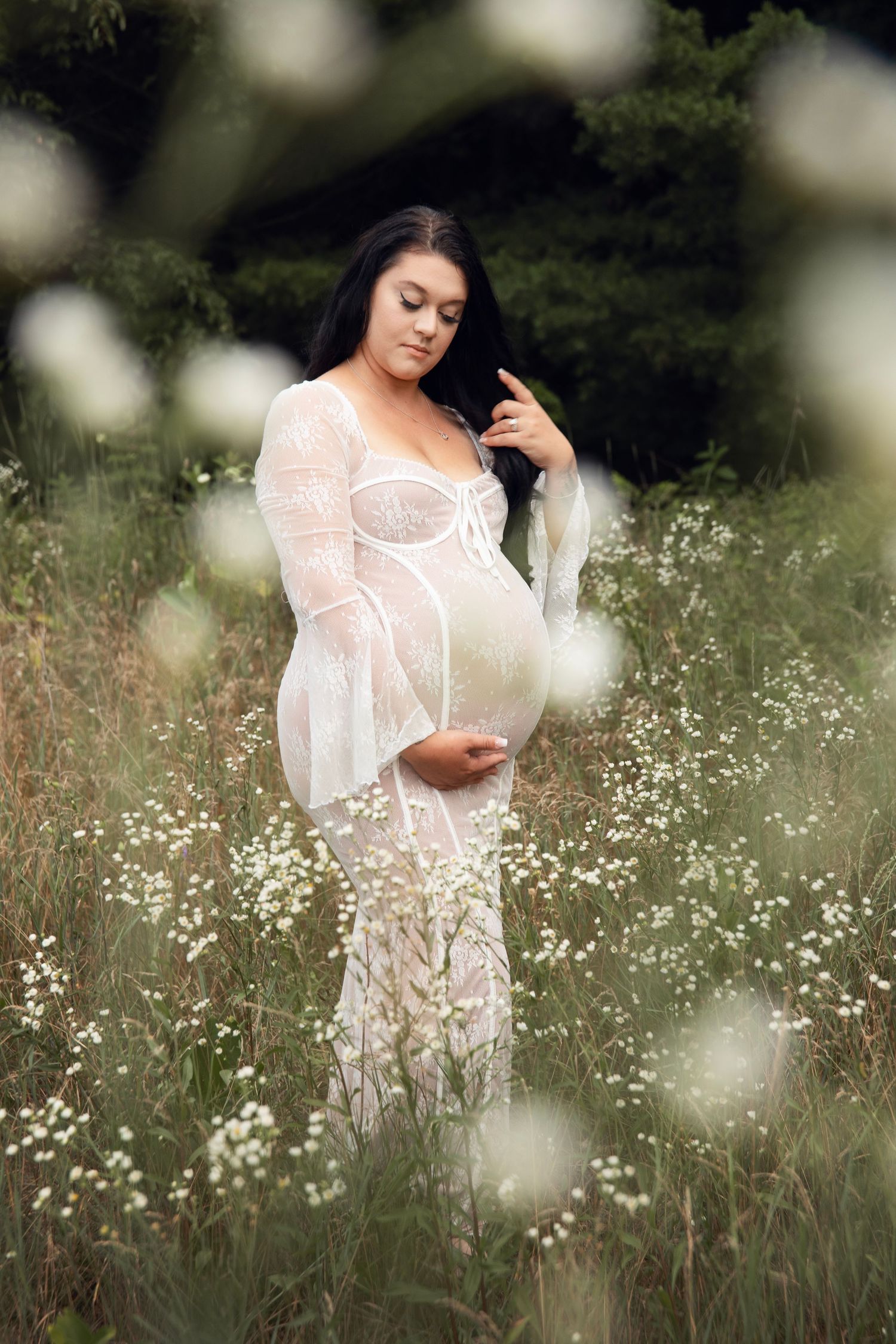 A person in a flowing white lace dress poses gracefully among delicate wildflowers in a dreamy outdoor setting.