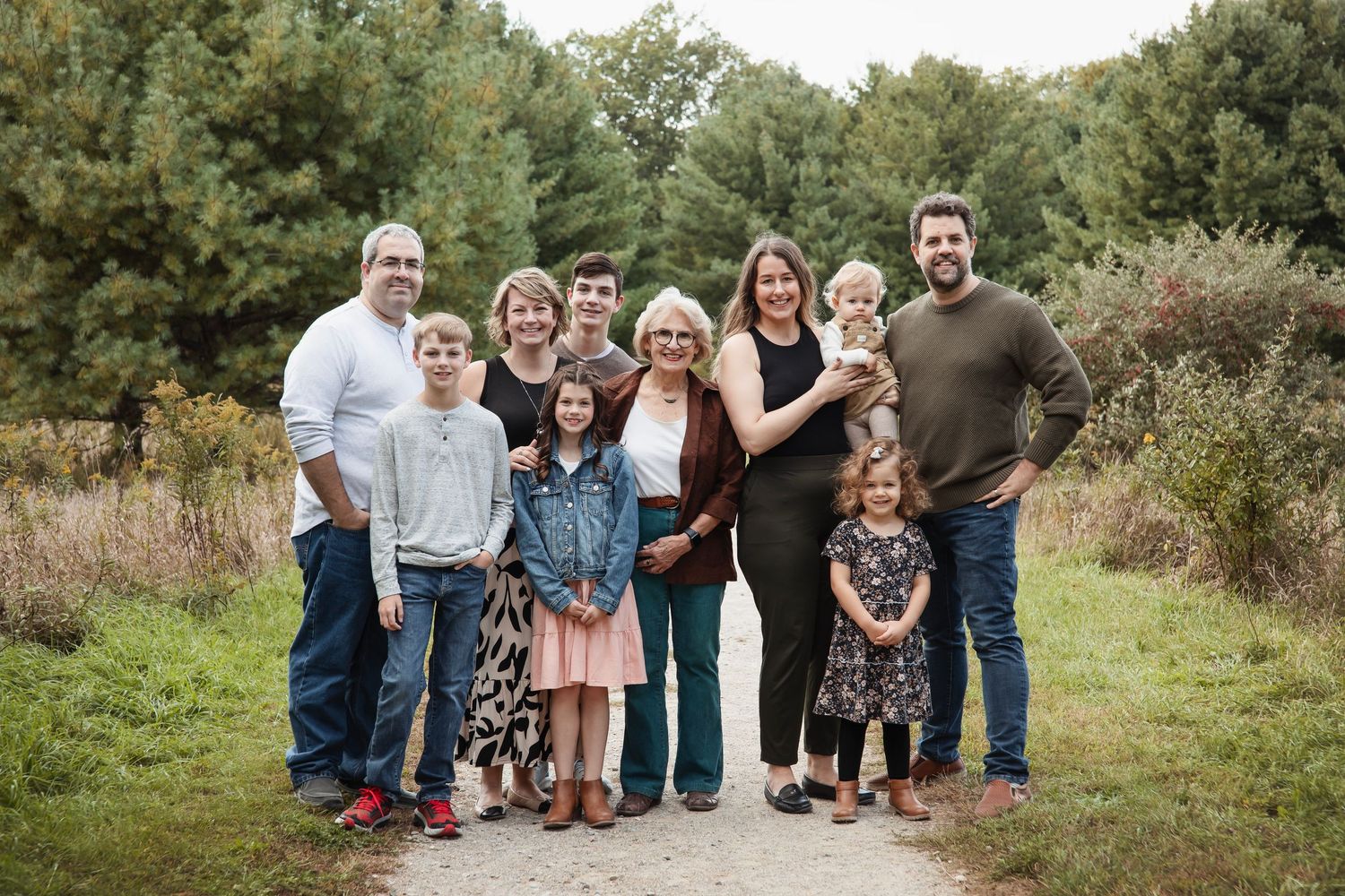 Multi-generational family poses together on a path surrounded by autumn foliage.