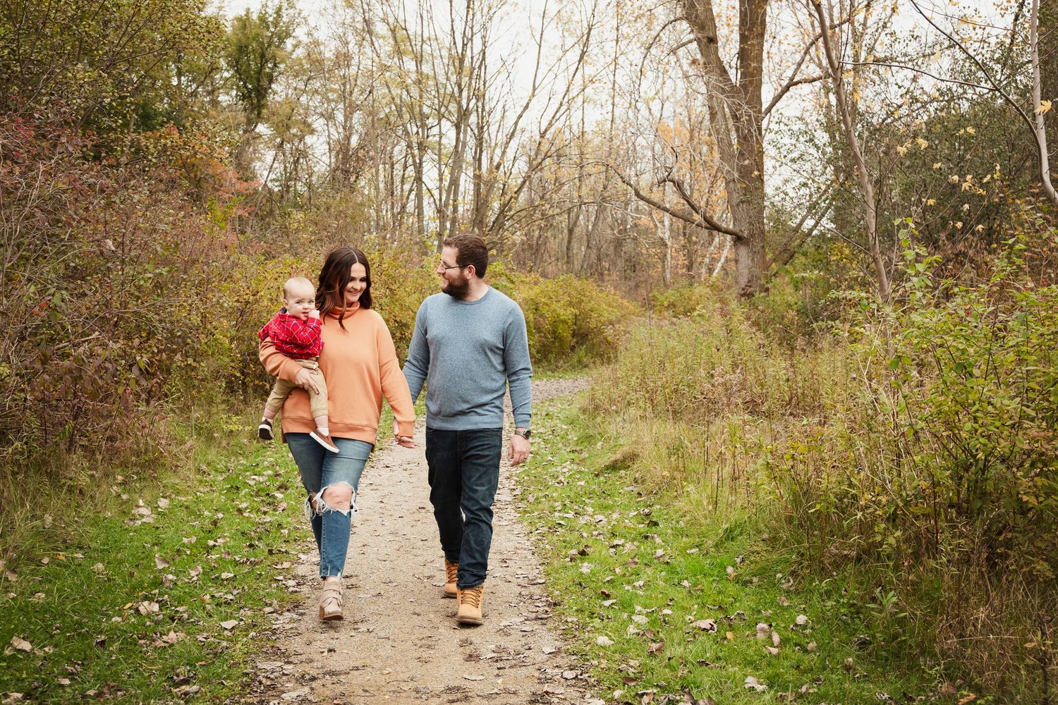 A couple walking down a wooded path surrounded by fallen leaves.