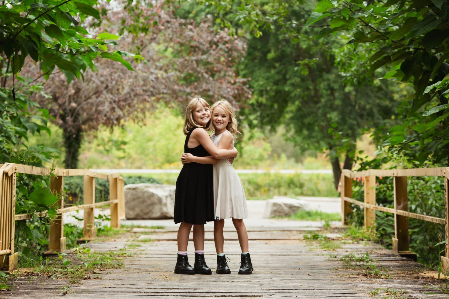 Two children in black and white dresses hugging on a wooden bridge.