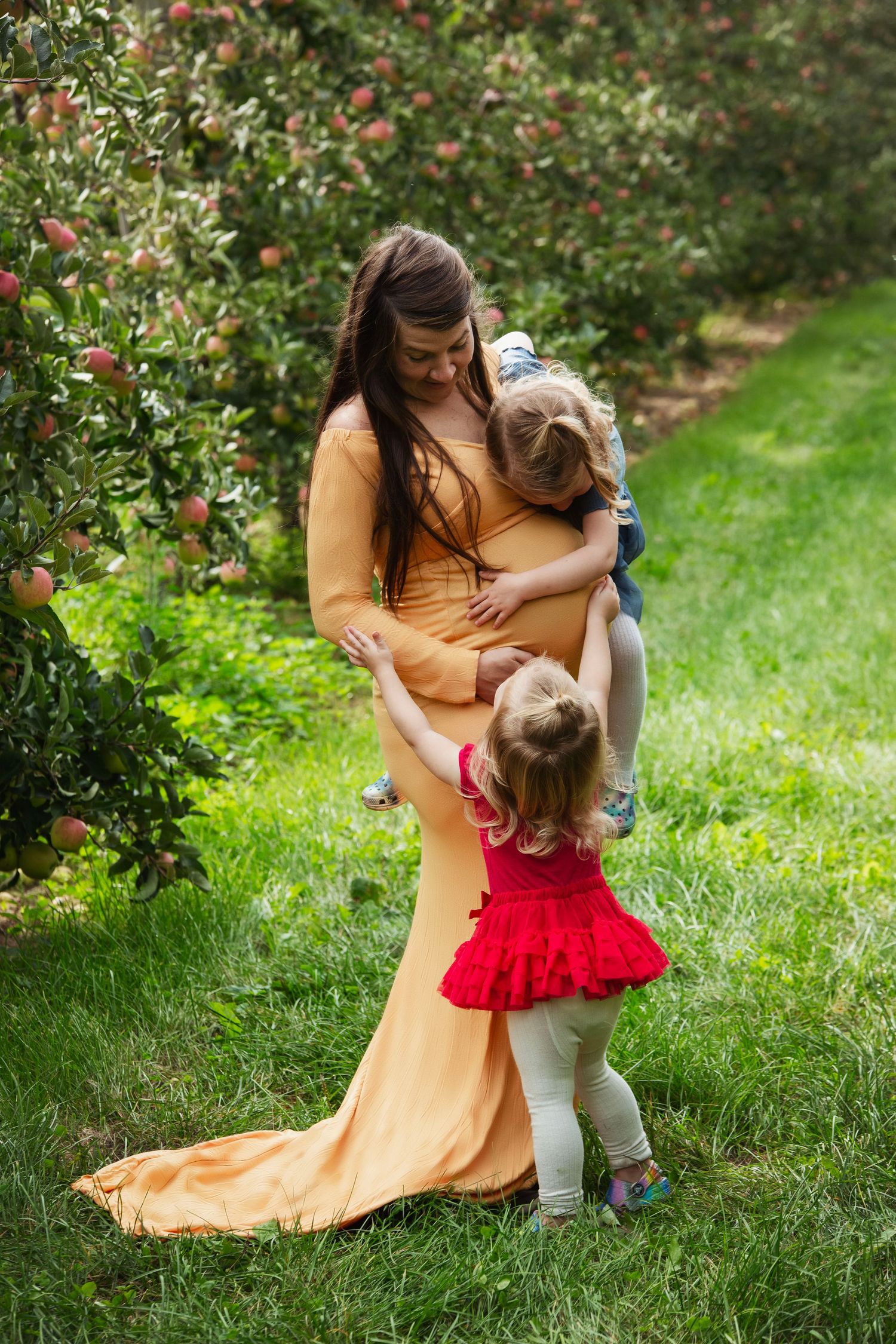Mother and child sharing tender moment in apple orchard wearing yellow dress and red outfit.