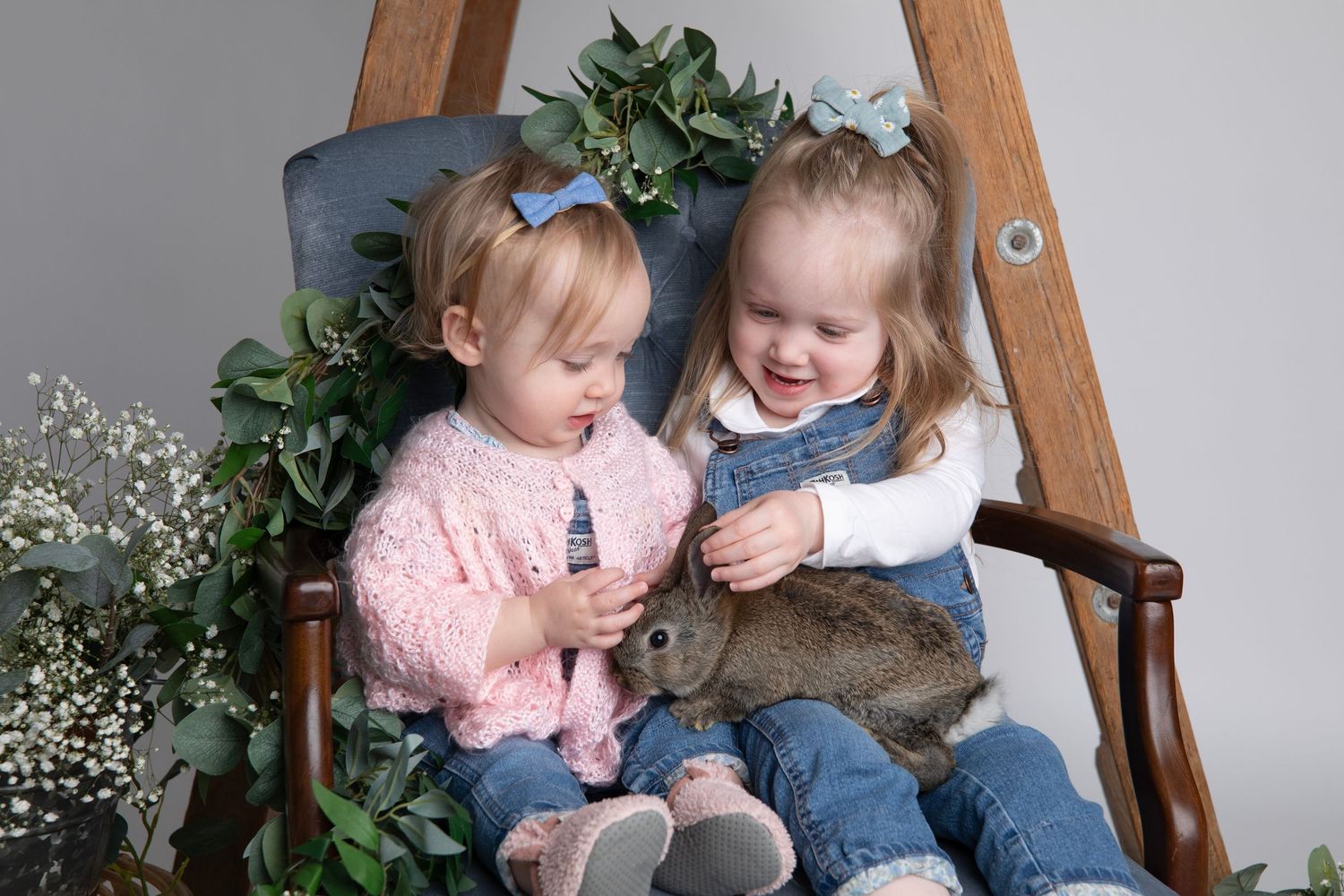 A series of candid shots showing two small children in denim and pink sitting on a wooden chair with foliage accents and a bunny for Easter.