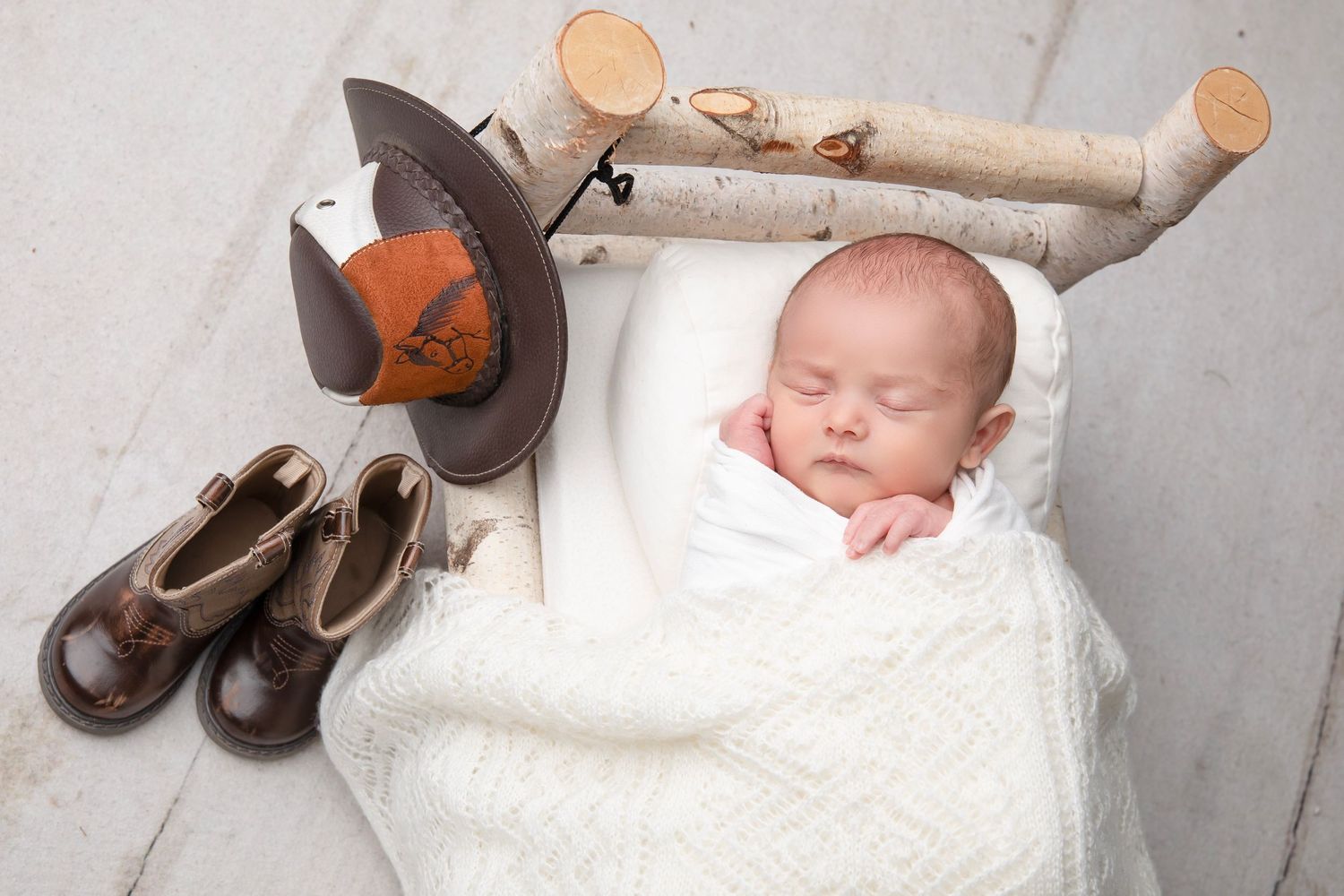 Sleeping baby in white swaddle next to rustic decor and boots.