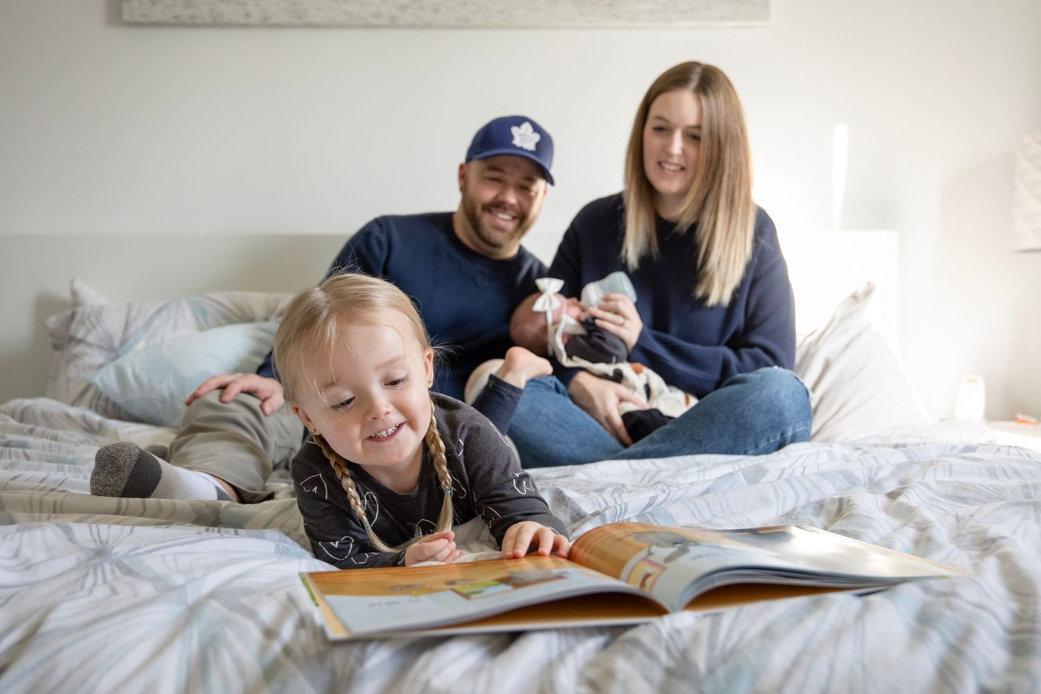 Family relaxing together on white bedding during casual lifestyle photo session.
