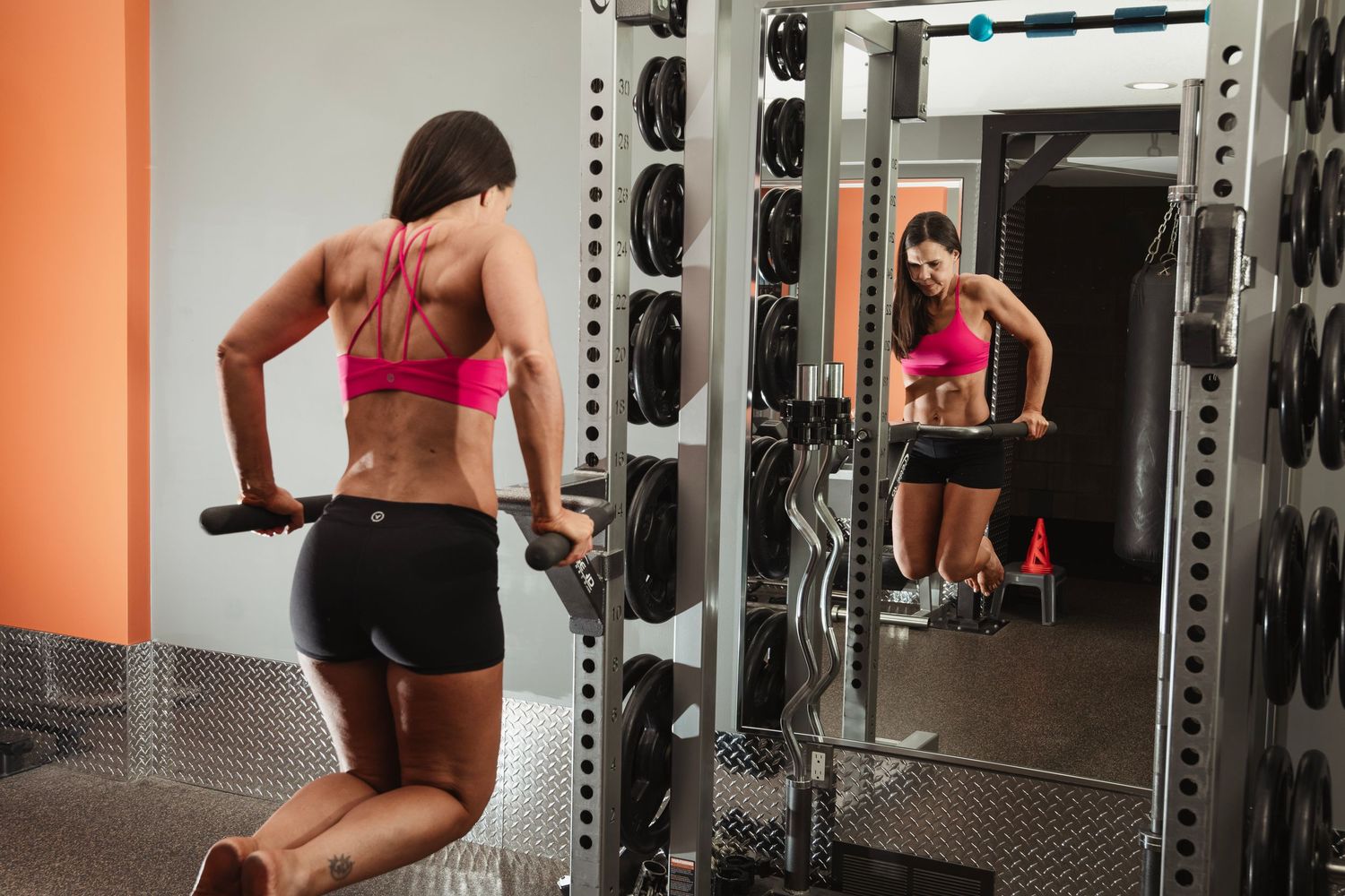 Athletic person performing dumbbell exercises in front of a gym mirror wearing pink sportswear and black shorts.