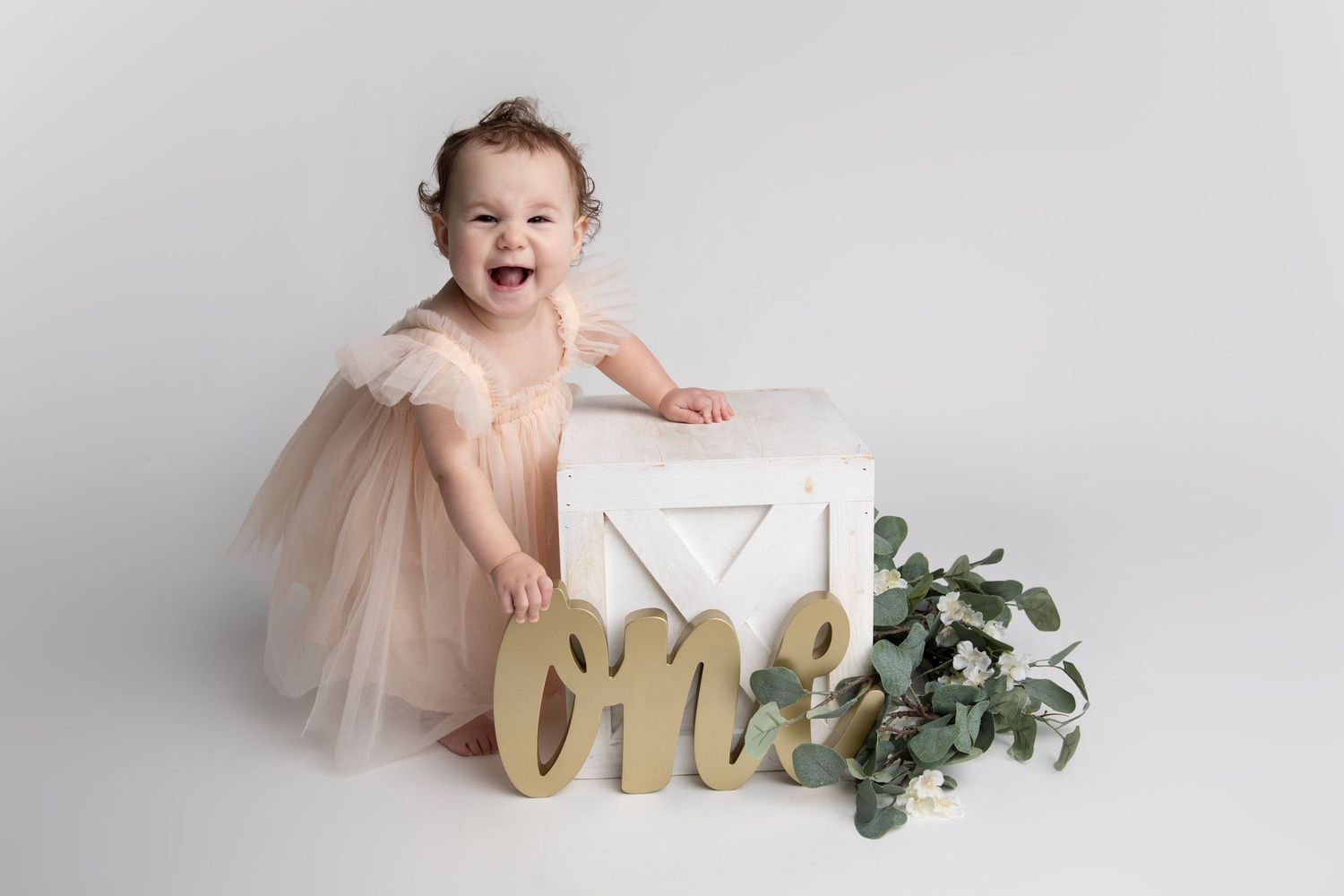 Sweet cake smash photography session with pink tulle dress and white decor against light grey backdrop.