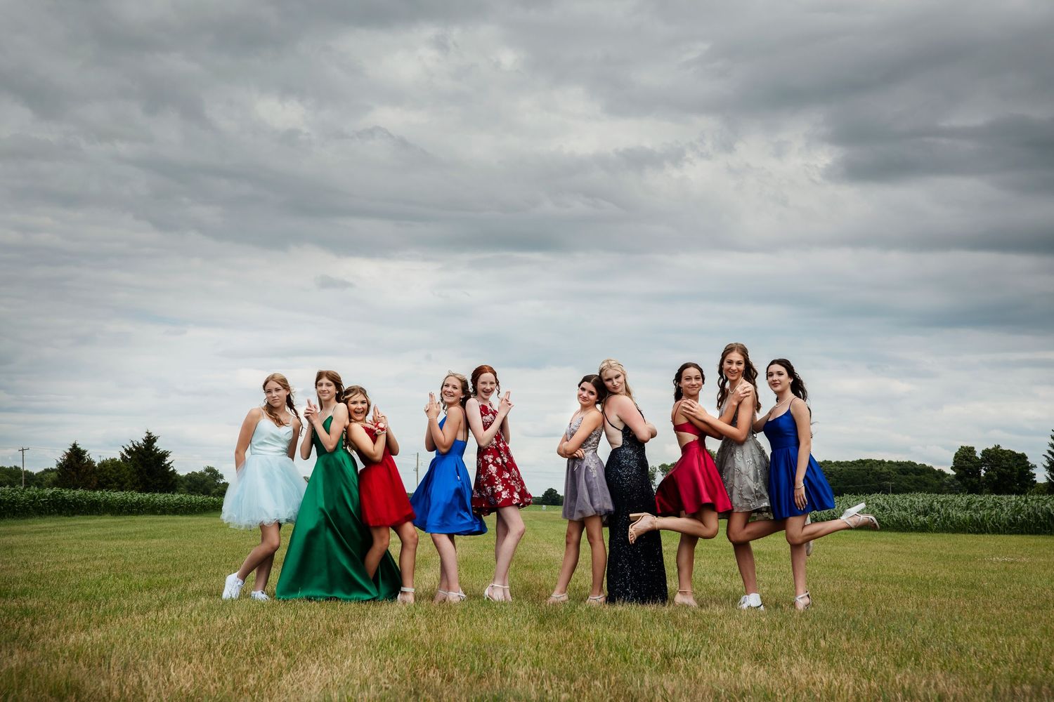 Group graduation photo series in a grassy field under dramatic cloudy skies.