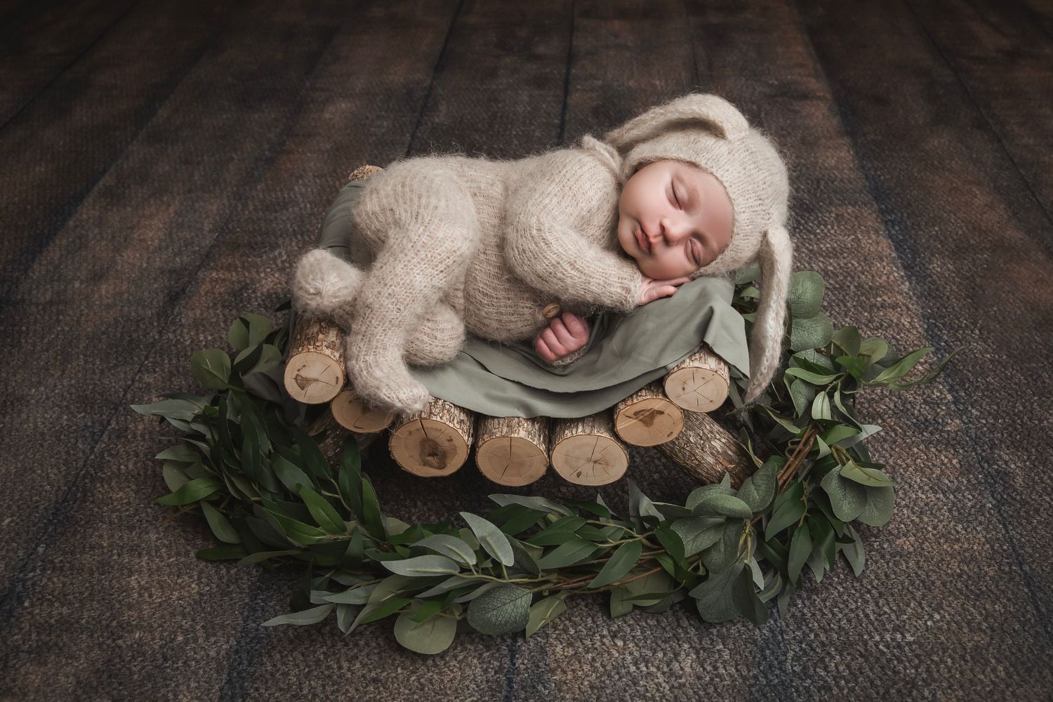 Newborn resting on wooden surface surrounded by greenery and natural decorative elements.