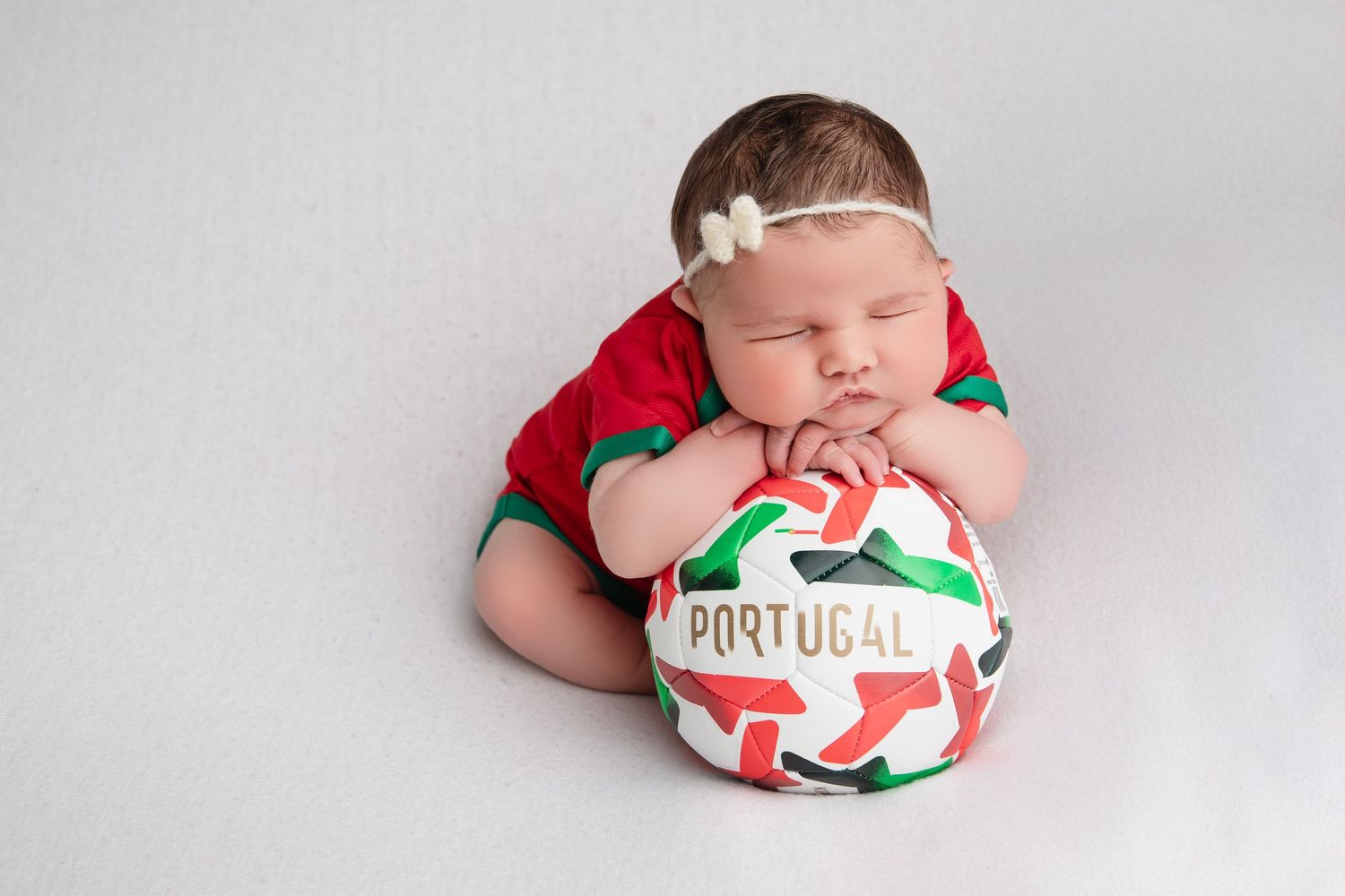 Newborn photography series featuring Portugal-themed sports attire and props.