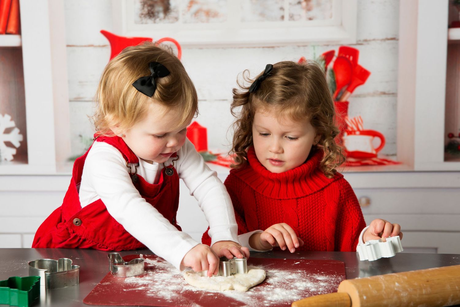 Children in red and white outfits roll out cookie dough together at a white counter during holiday baking.