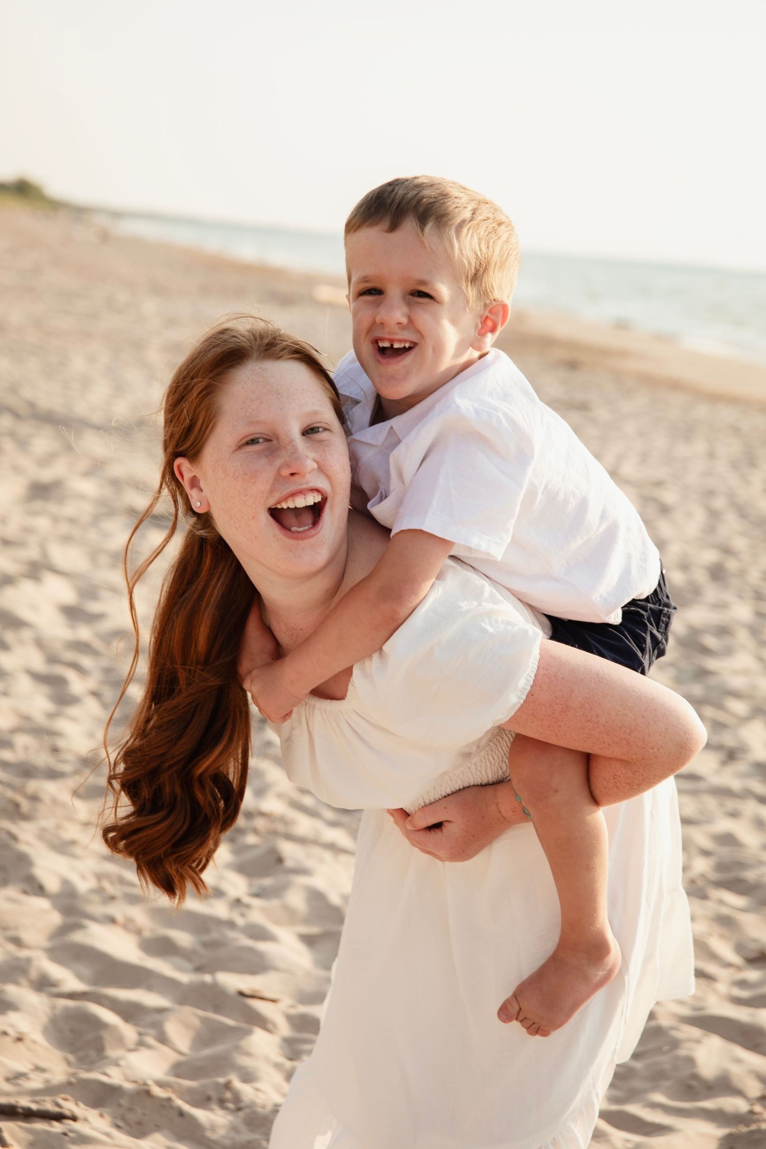 A mother and child play joyfully together on a sandy beach during a warm sunny afternoon.