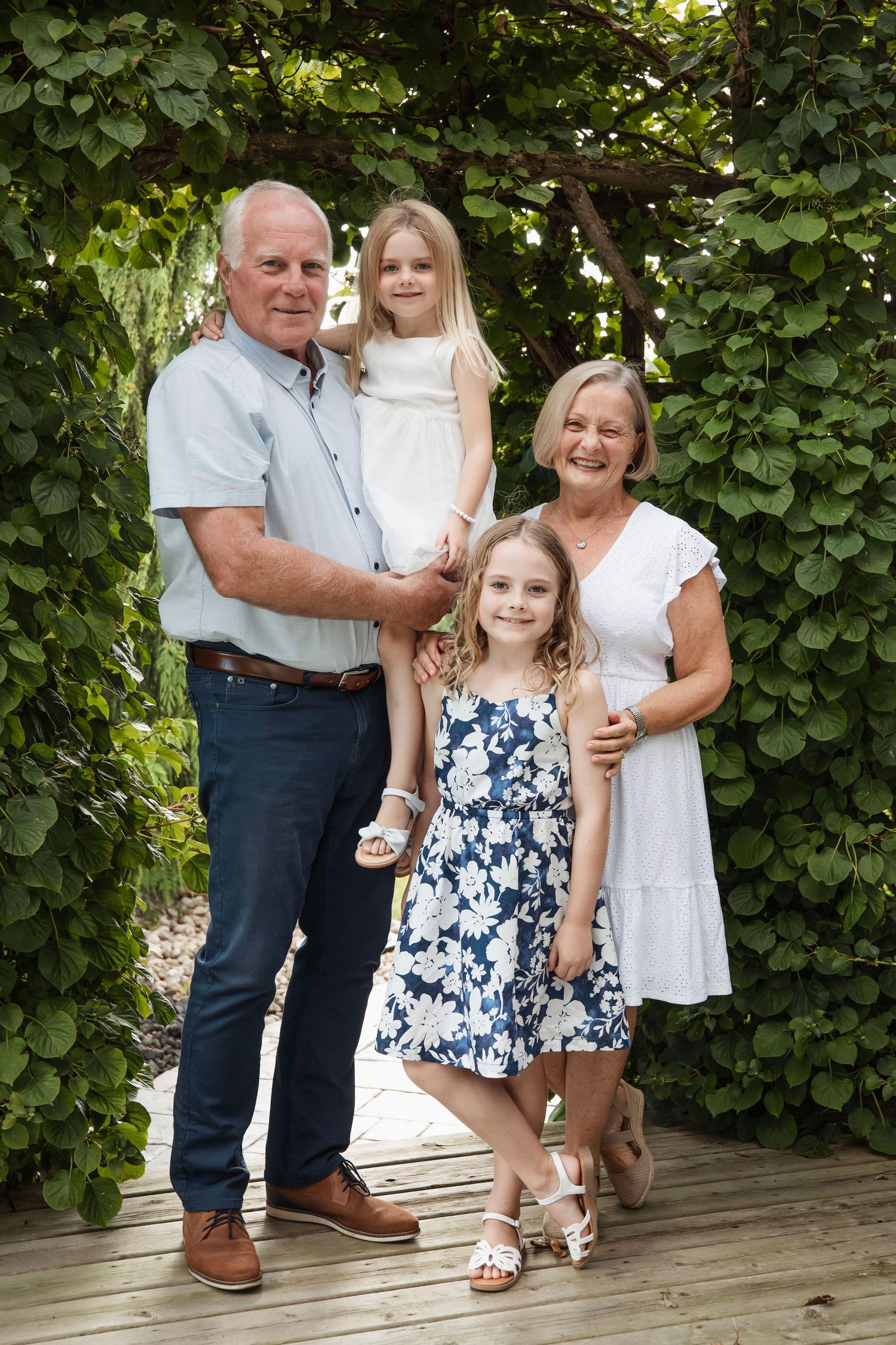 Family members pose together on a wooden deck surrounded by lush green vines.