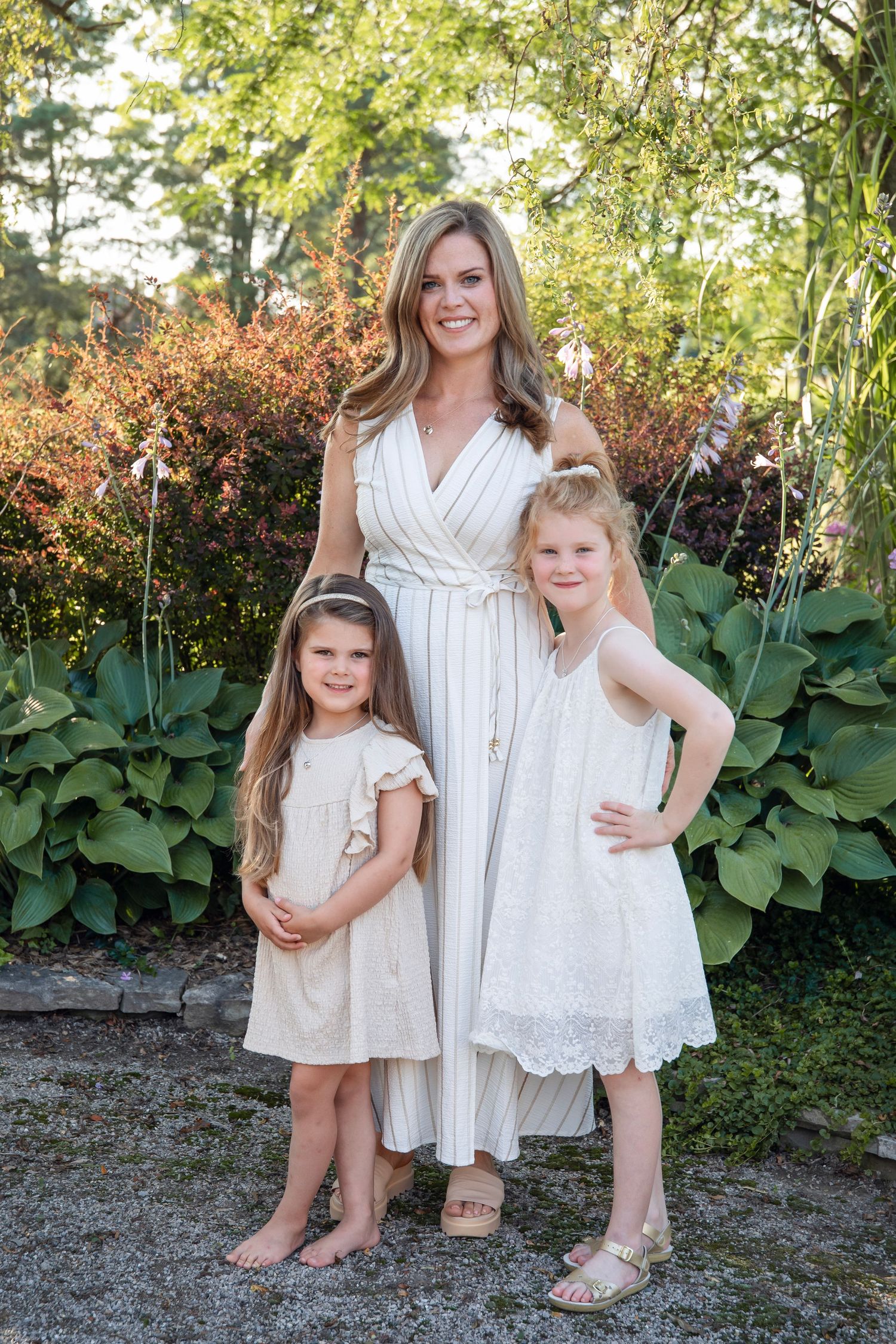 Family wearing coordinated white outfits poses together in front of lush garden backdrop.