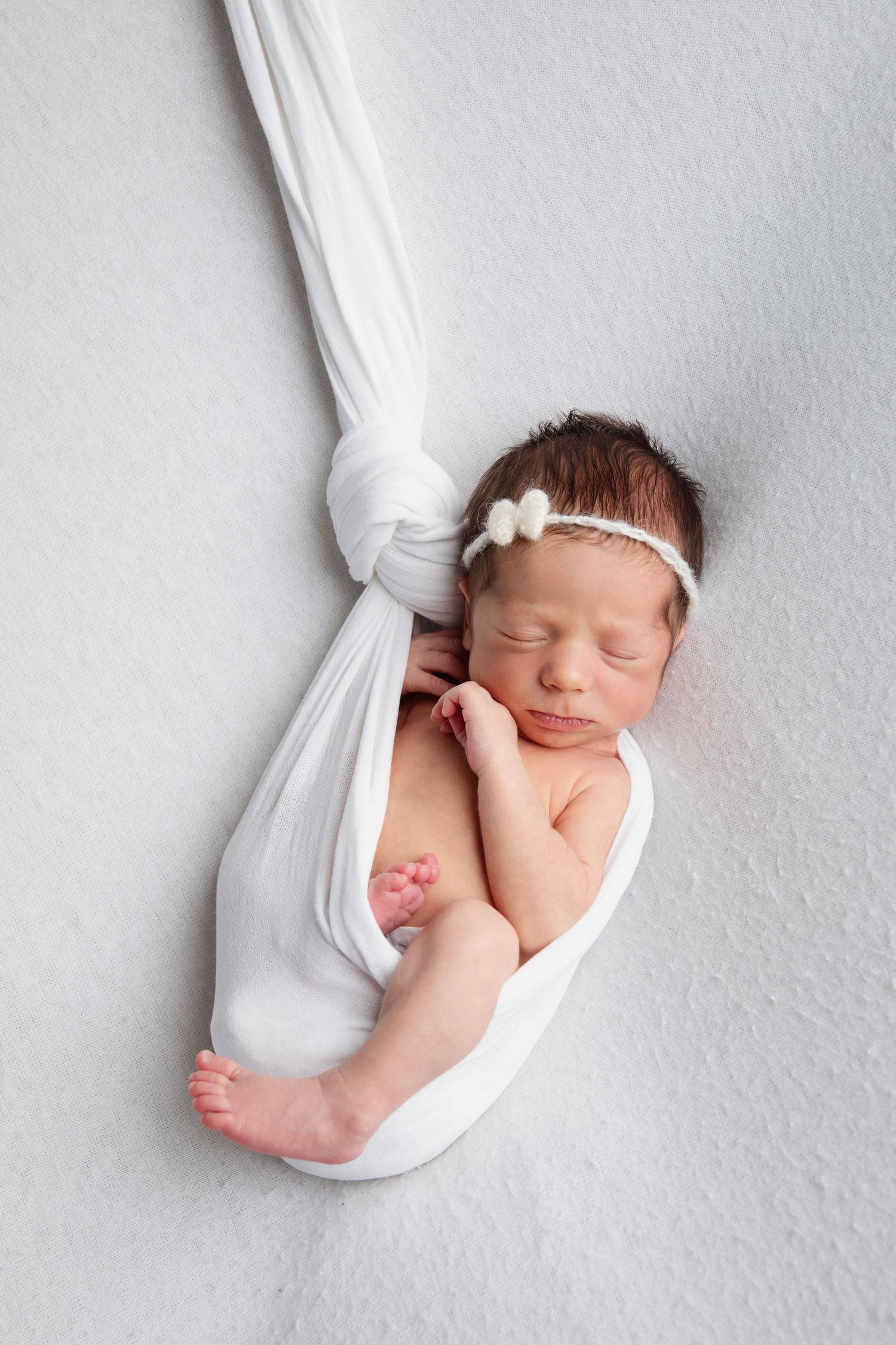 Sleeping newborn wrapped in soft white fabric against light gray background in minimalist style.