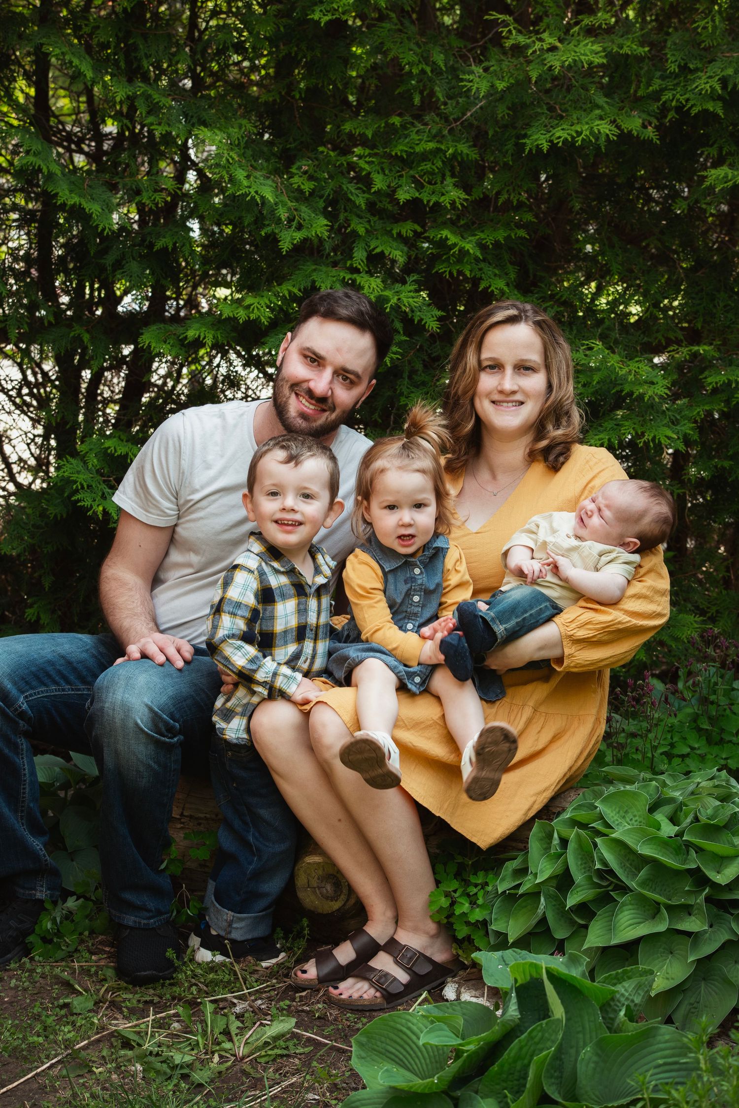 Family sitting together on garden steps surrounded by green foliage.