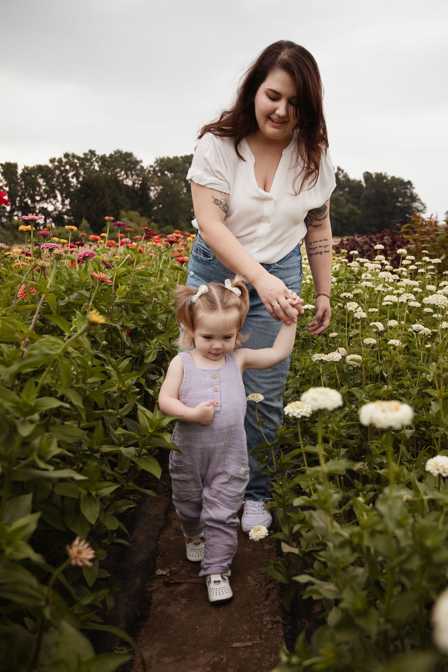 Parent and toddler walking through blooming flower garden on dirt path.