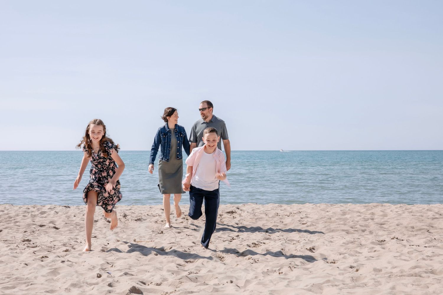 Family members walking together and playing on a sunny beach with ocean waves in background.
