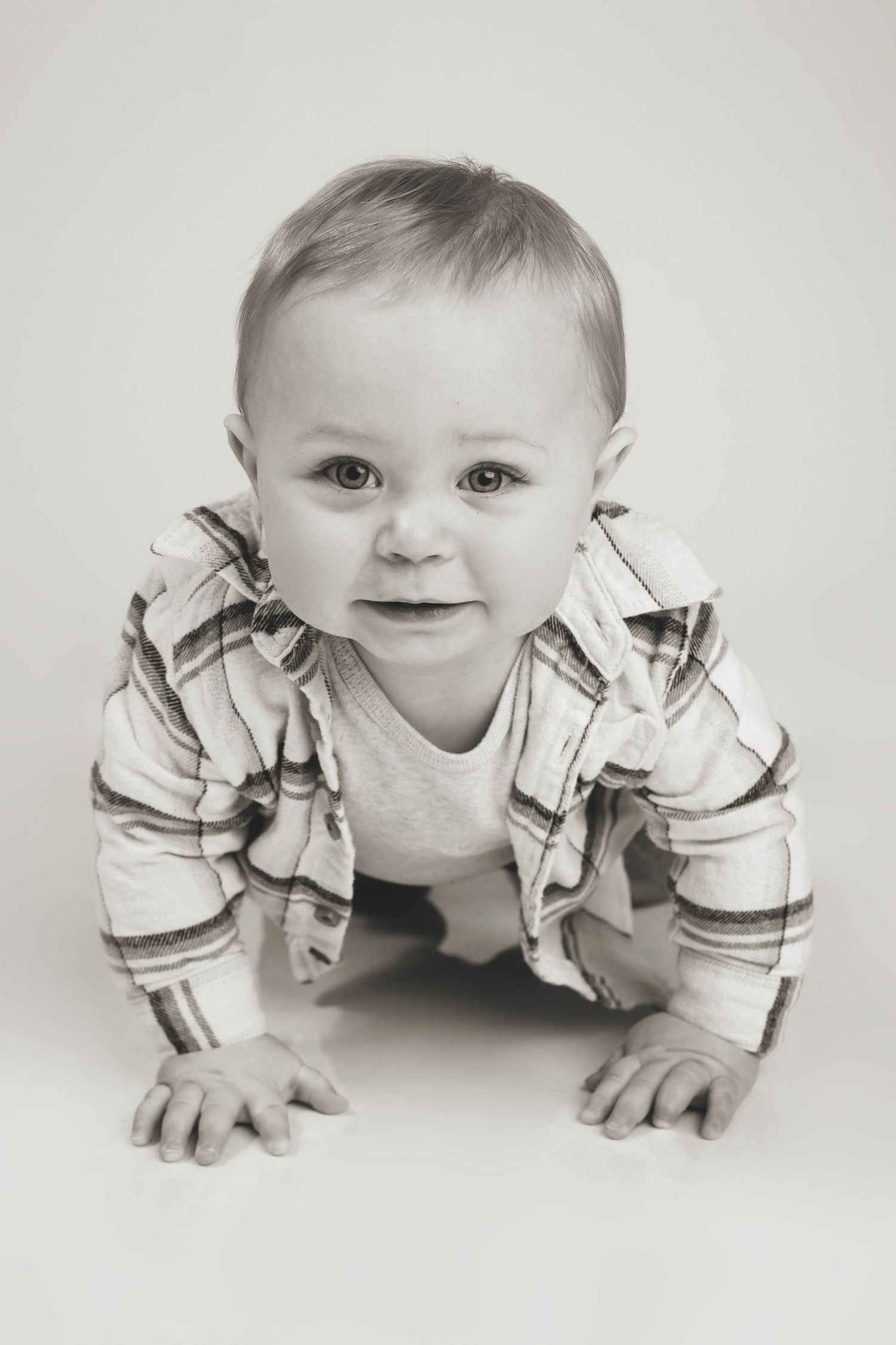 Baby in striped shirt crawling and smiling during black and white portrait session.