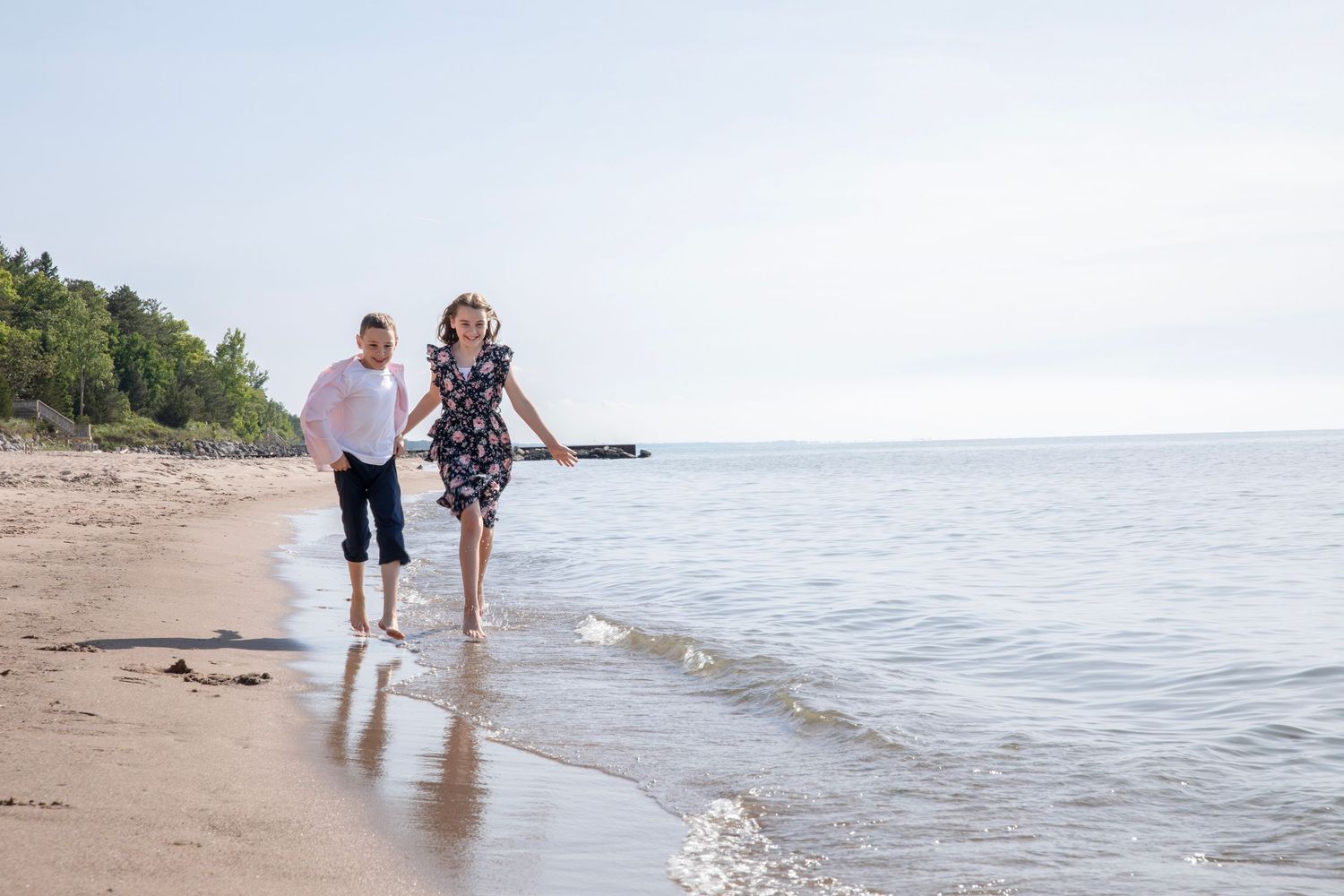 Beachside photo showing people walking along the shoreline with waves lapping at their feet.