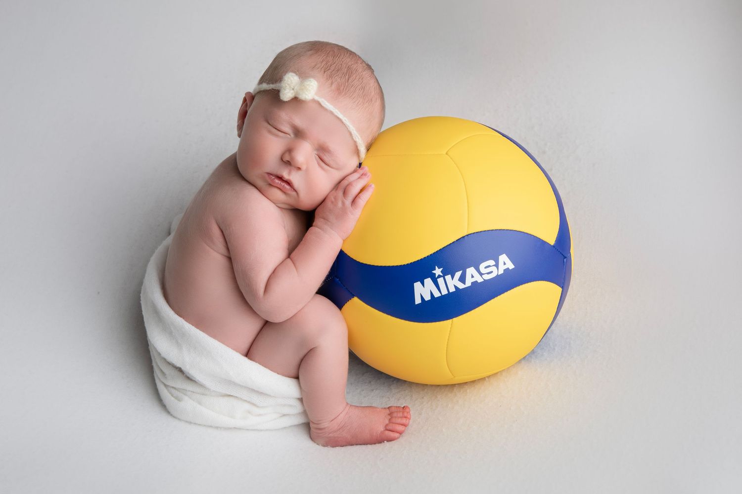 A series of four artistic newborn baby photos with a yellow and blue volleyball as a prop in a studio setting.