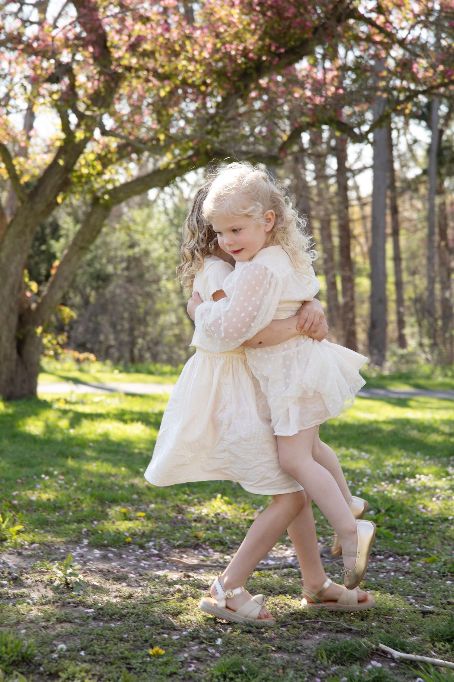 Children in white dresses playing together in sunlit spring garden.