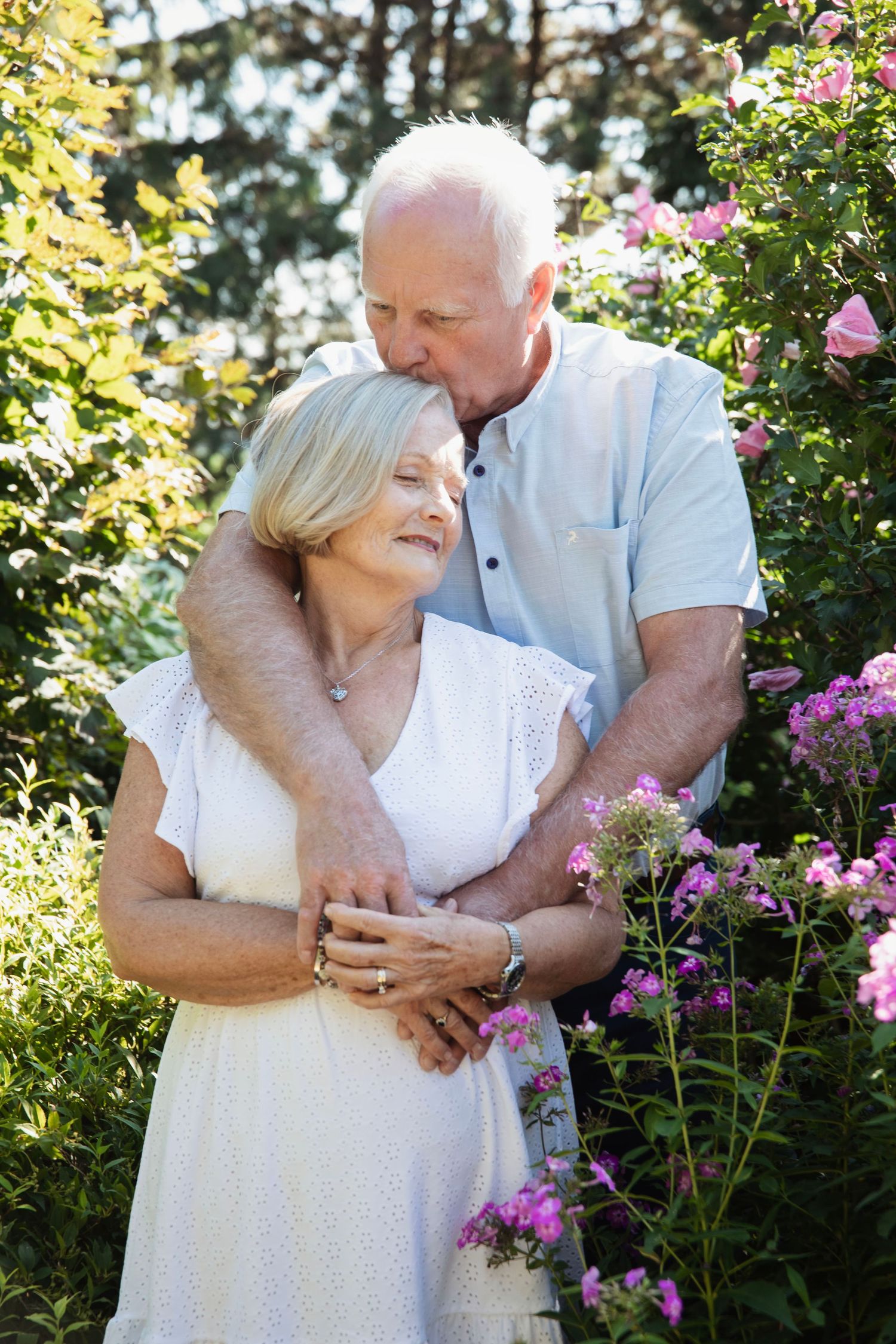 Romantic couple share intimate moments among blooming pink flowers in a garden setting.