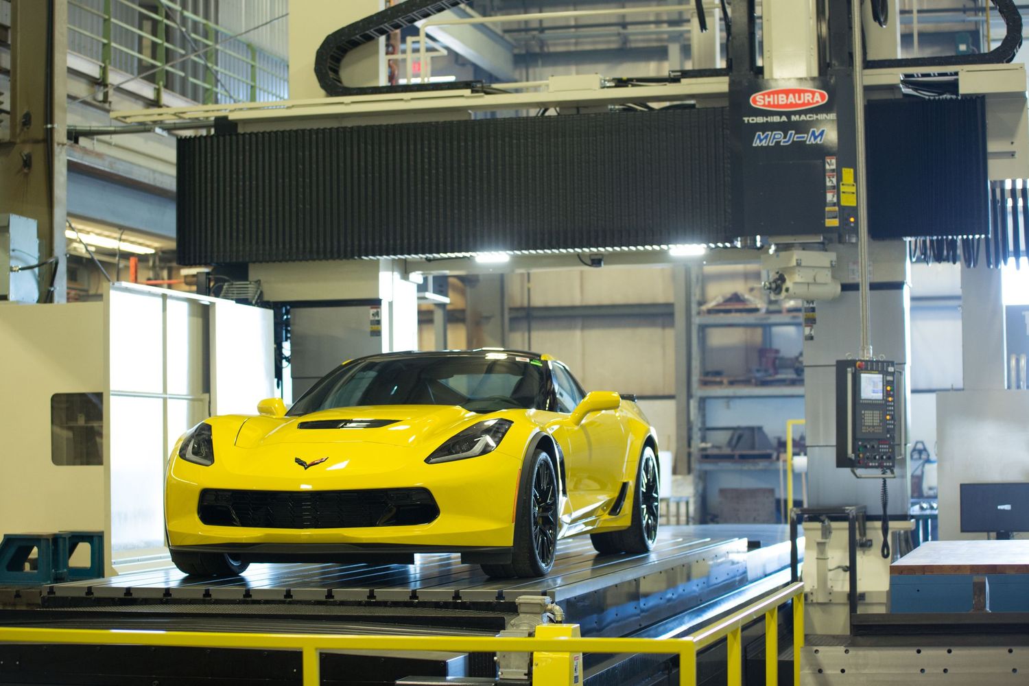 Yellow Corvette C7 Z06 sports car displayed at an indoor showroom with its hood open and bright lighting.