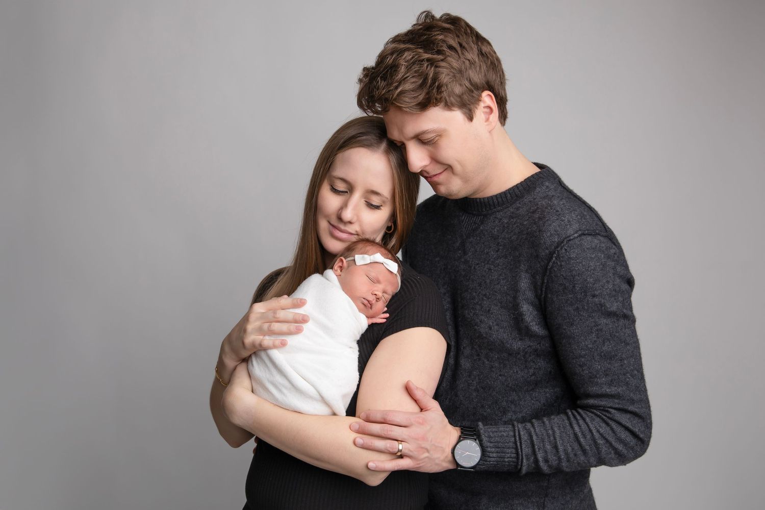 Parents sharing tender moment with newborn in studio setting against gray background.