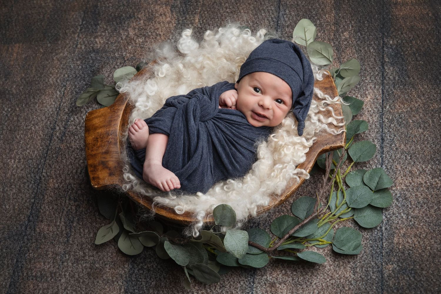 Sleeping baby on textured blanket surrounded by green eucalyptus leaves.