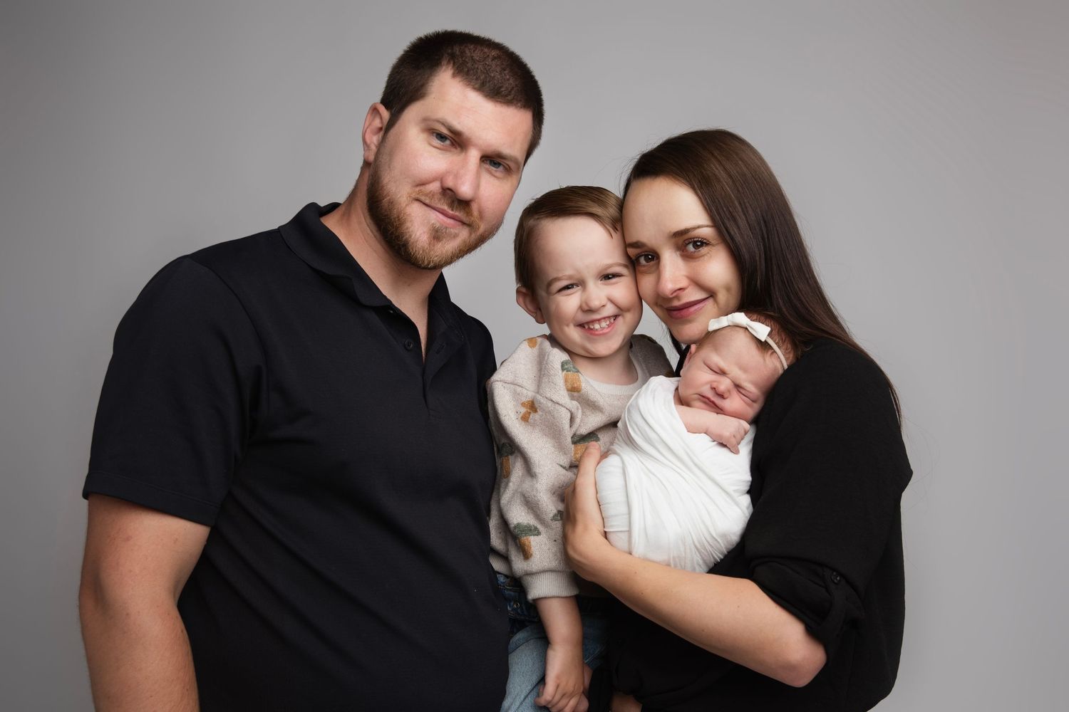 Family wearing black and white coordinated outfits poses together for professional studio portraits.