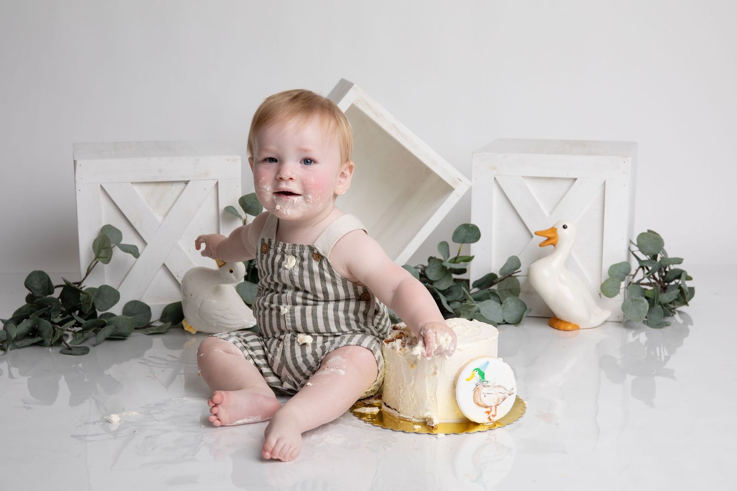 1st birthday Milestone photo session featuring props, greenery, and striped baby outfit along with a custom naked cake and duck accents.
