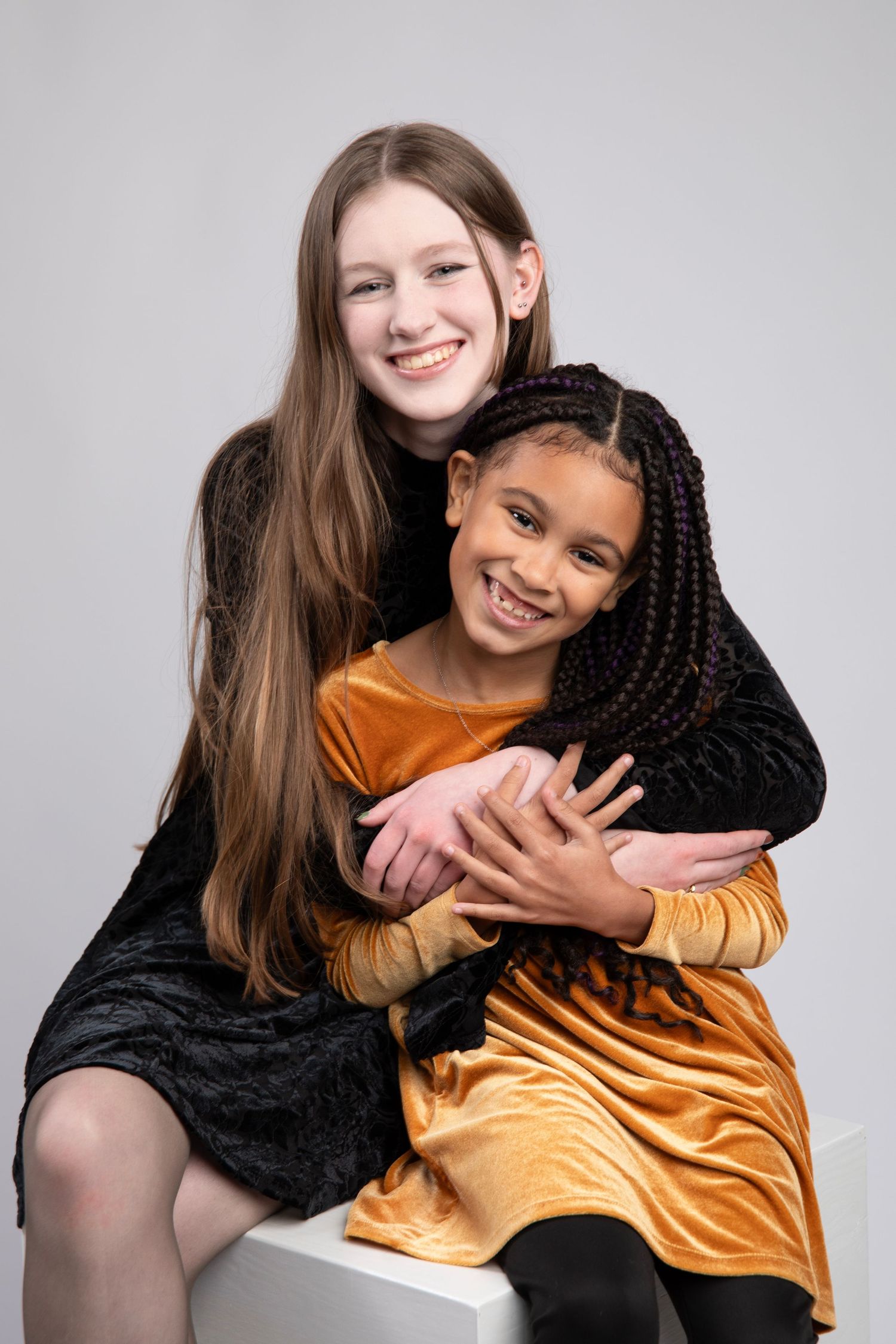 Two friends in contrasting black and gold outfits share a warm embrace while posing together for photos.