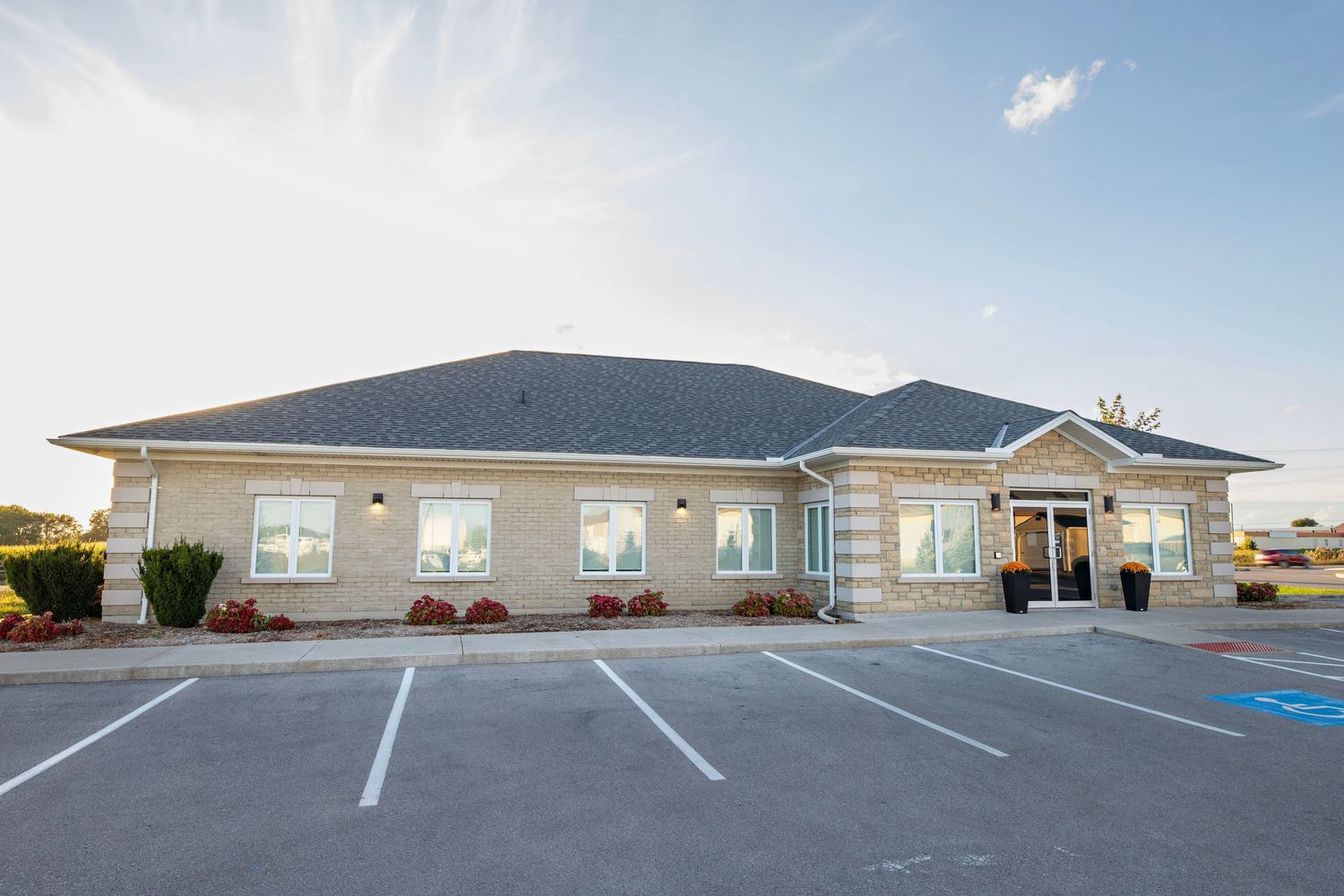 Modern beige medical office building with black roof and empty parking spaces during sunny day.