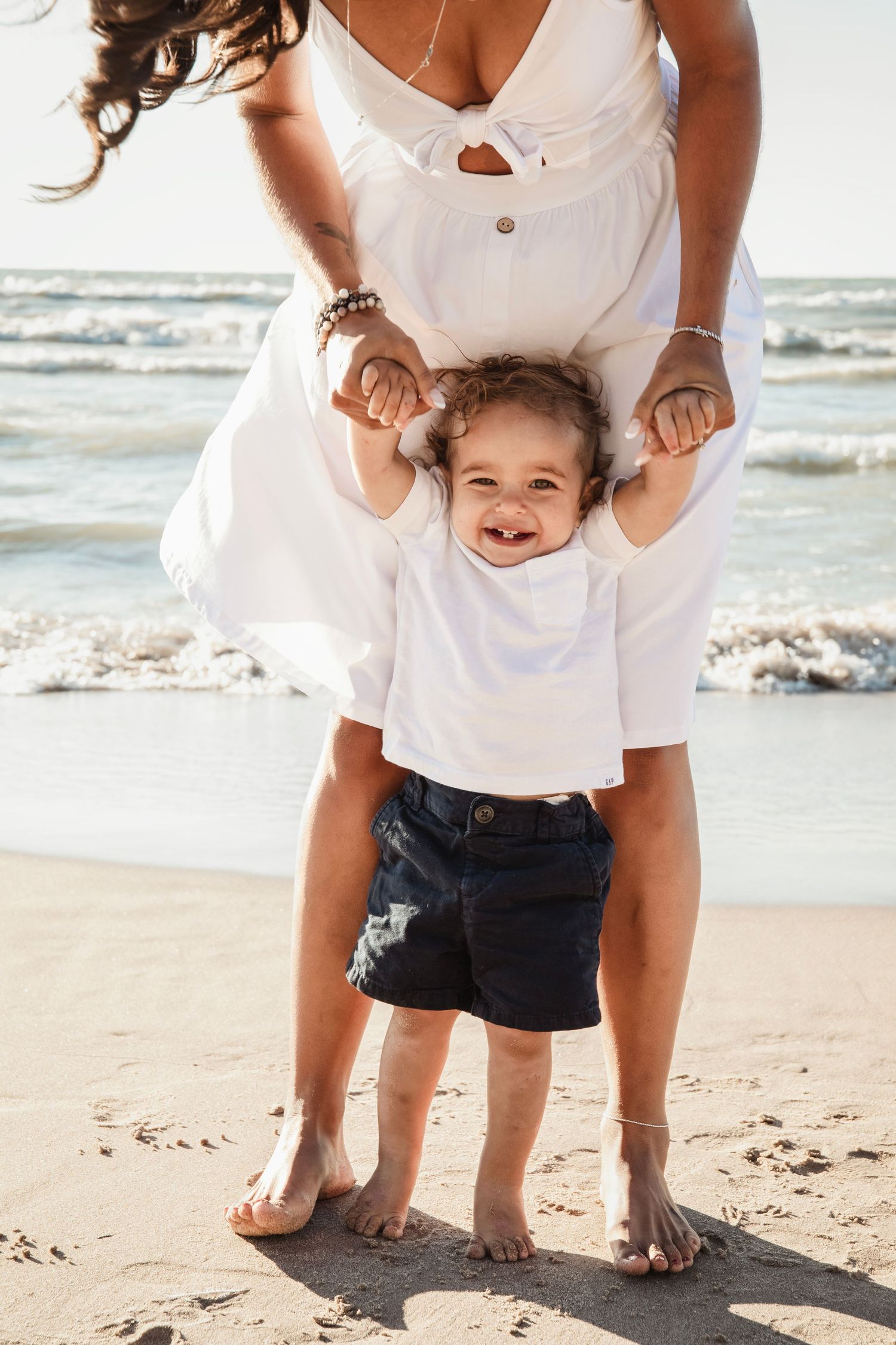 Fun beach moment captured as parent holds child's hands while standing in sand.