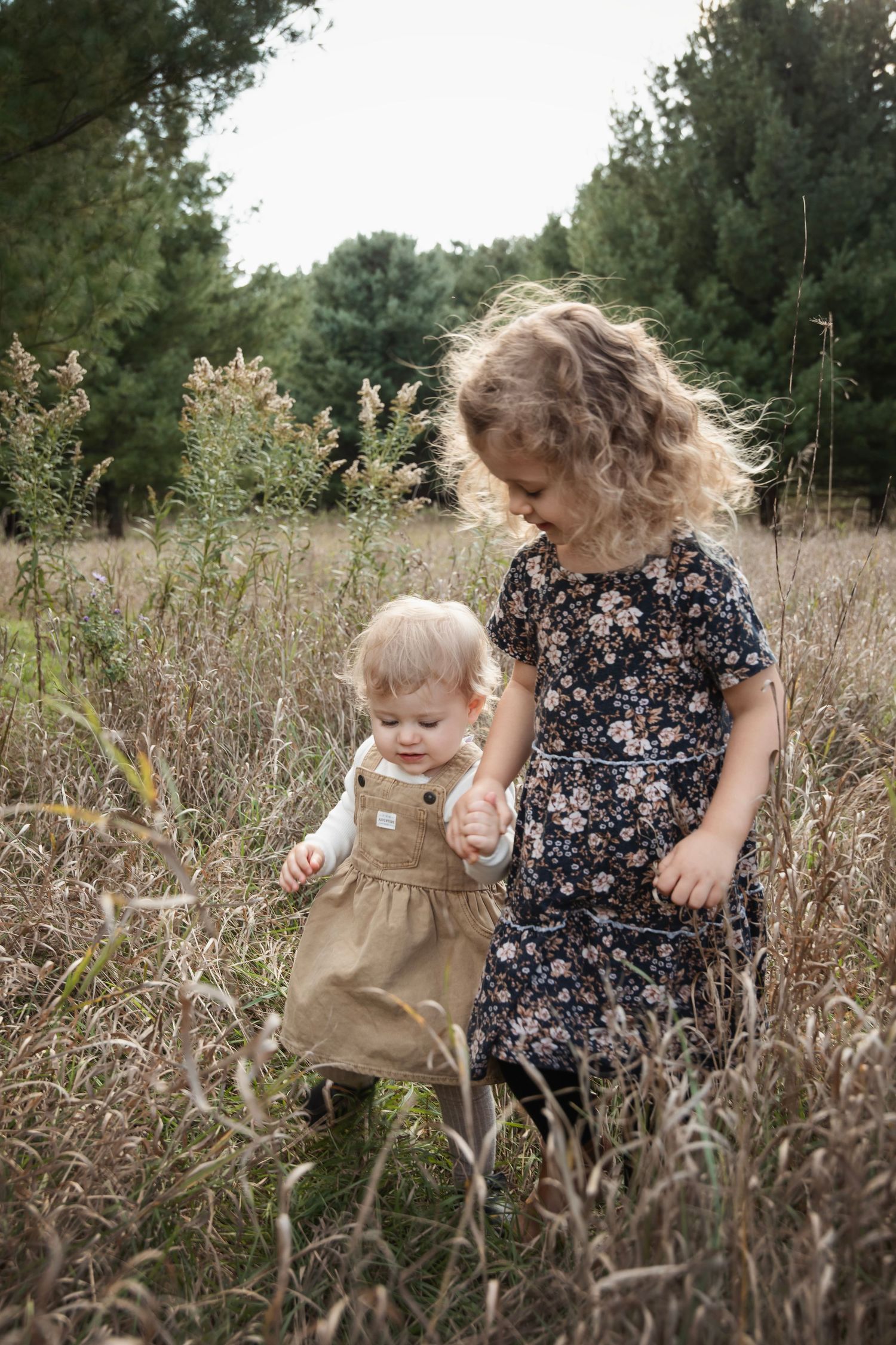 Two children in floral dresses playing together in a field of tall grass.