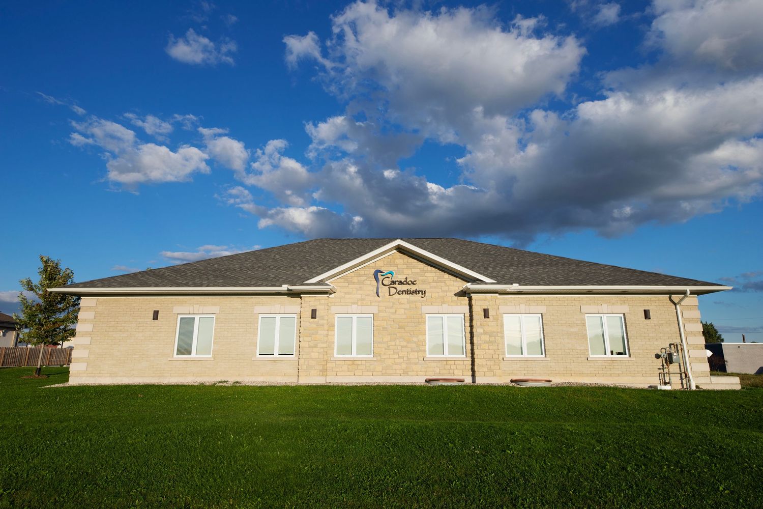 Row of single-story beige modular buildings under bright blue sky with scattered white clouds and utility poles.