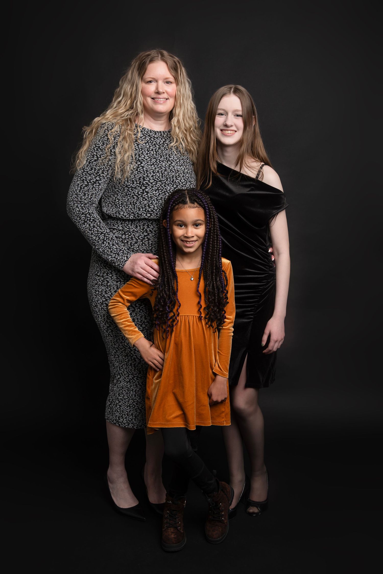 Three people pose together against a dark background wearing contrasting orange and black dresses.