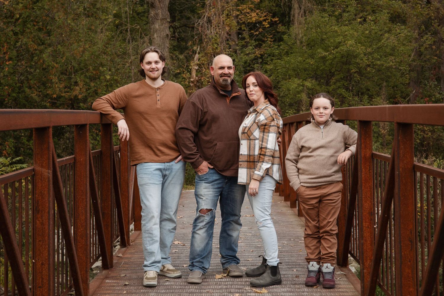 Family of four standing together on a wooden bridge in an autumn forest.