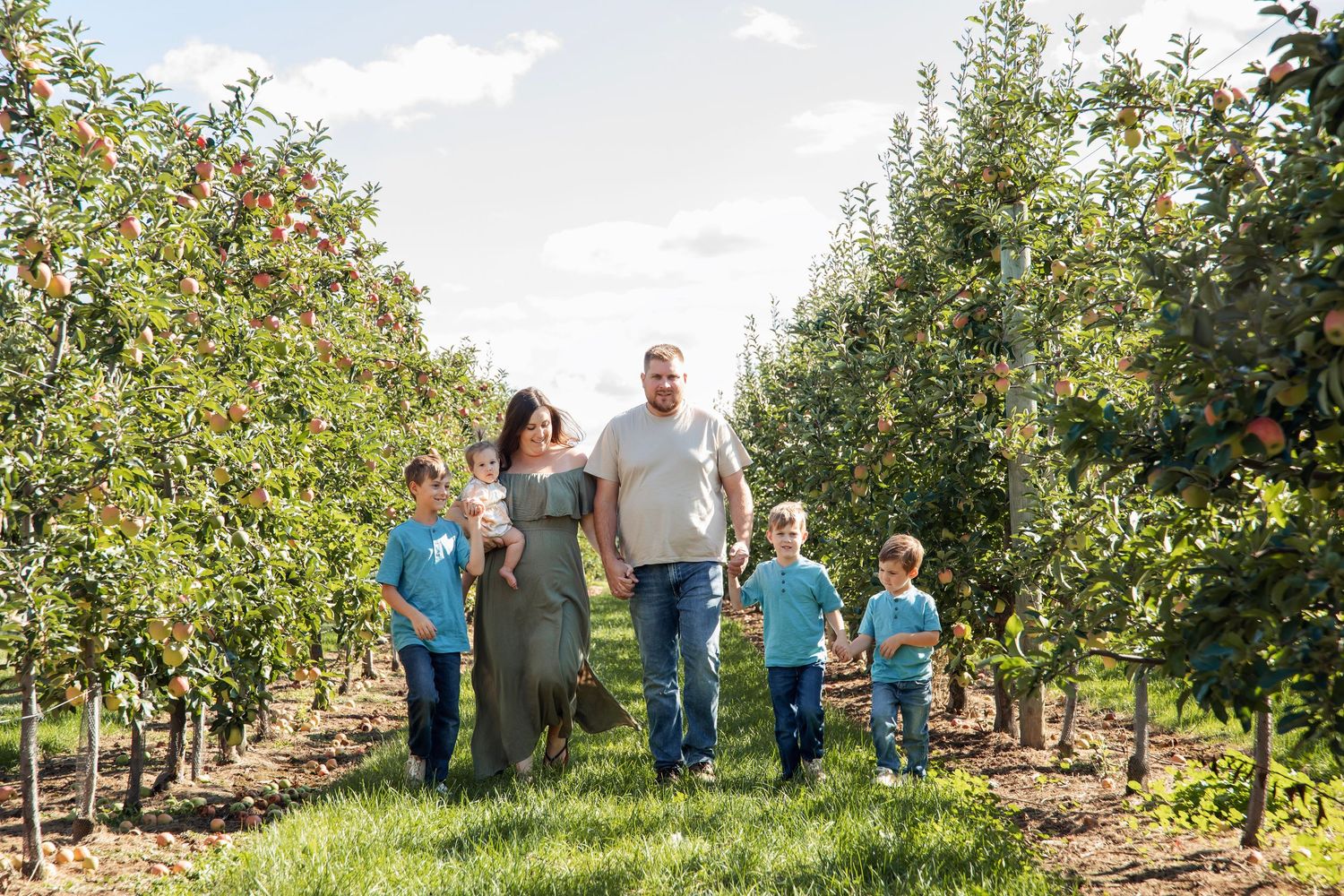 Landscape shot of an extended family group walking through rows of apple trees in a scenic orchard.