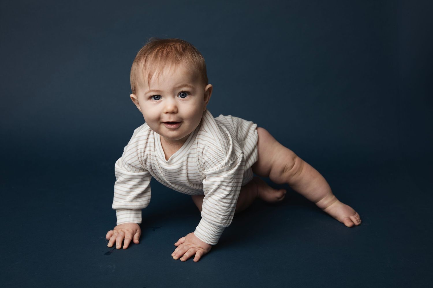 A baby in a cream-colored sweater crawls along a dark blue surface, shown from multiple angles and positions.