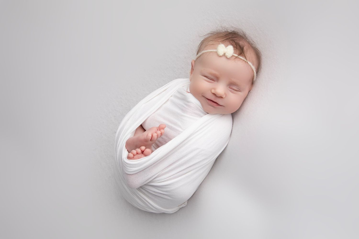 Professional newborn photography series showing baby wrapped in white against light backdrop.