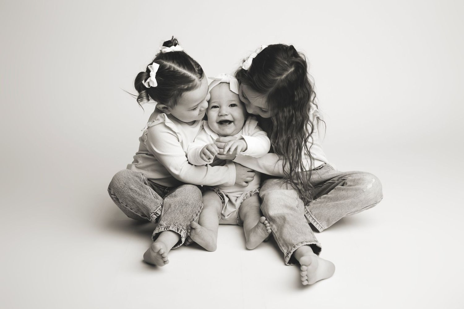 Two small children in white clothing sit facing each other on a light gray background in playful poses.