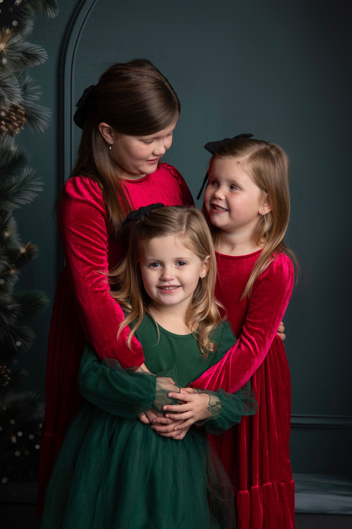 Two children wearing festive holiday dresses in red and green pose together against a dark background.
