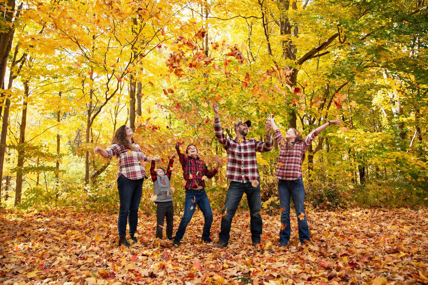 Group jumping joyfully among fall foliage wearing matching plaid shirts in an autumn forest setting.