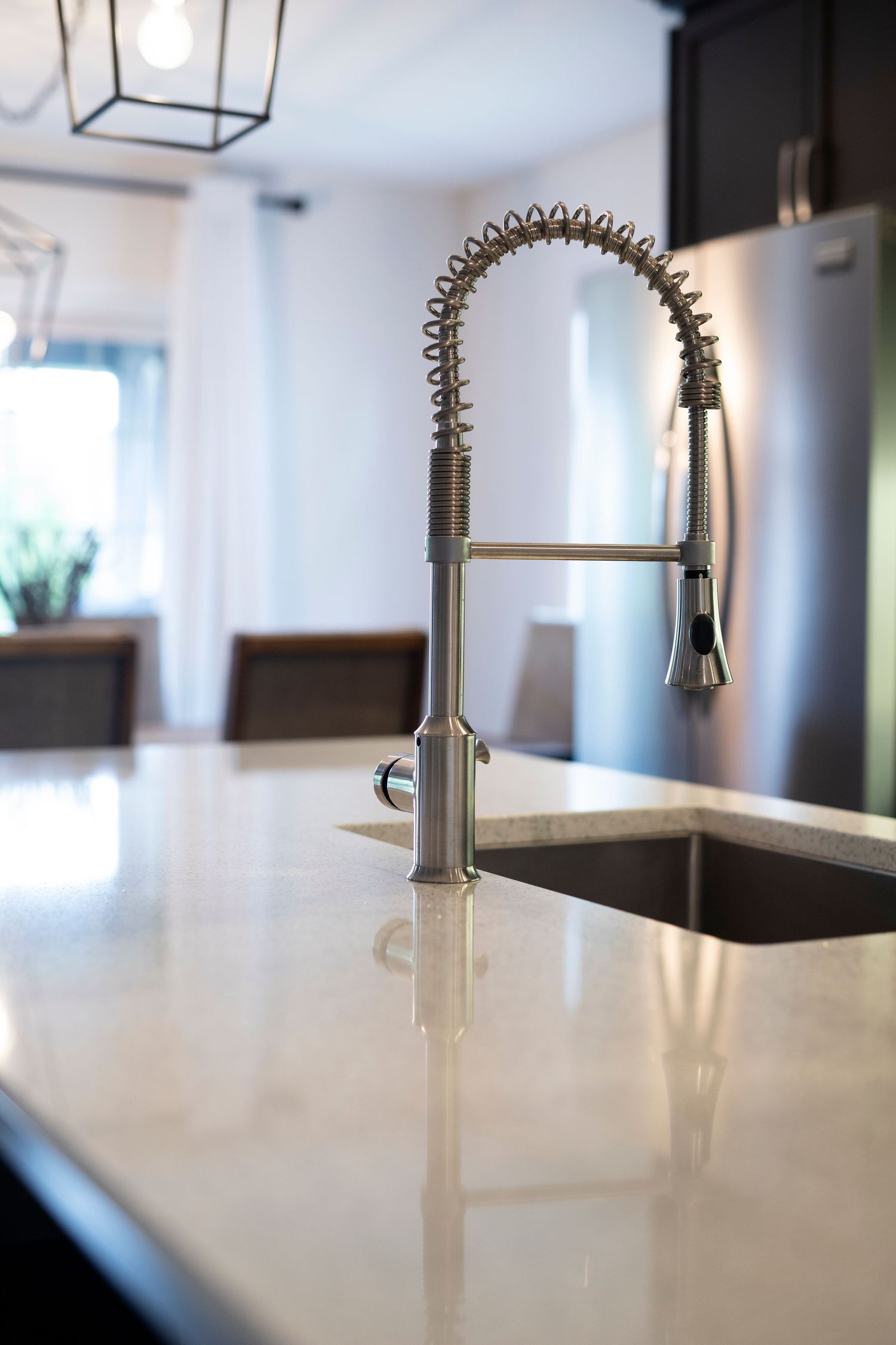 Modern kitchen features a sleek industrial style faucet with pull-down sprayer against white quartz countertop in sunlit room.