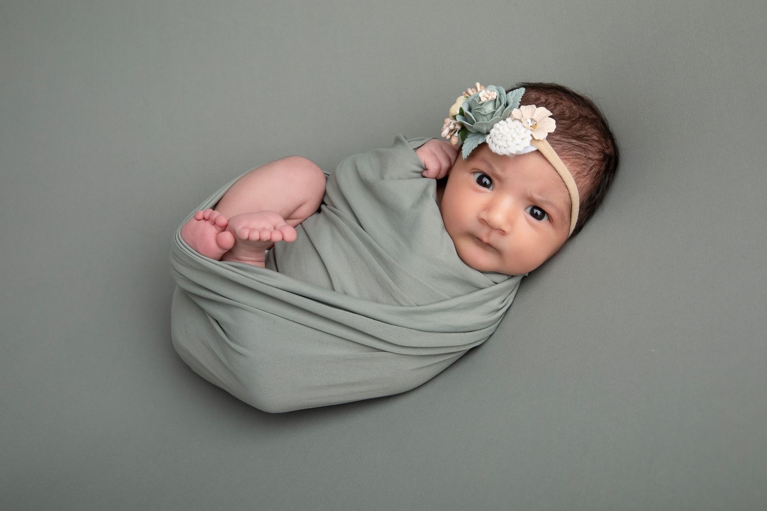 Newborn photo series with baby wrapped in soft grey swaddle against neutral background.
